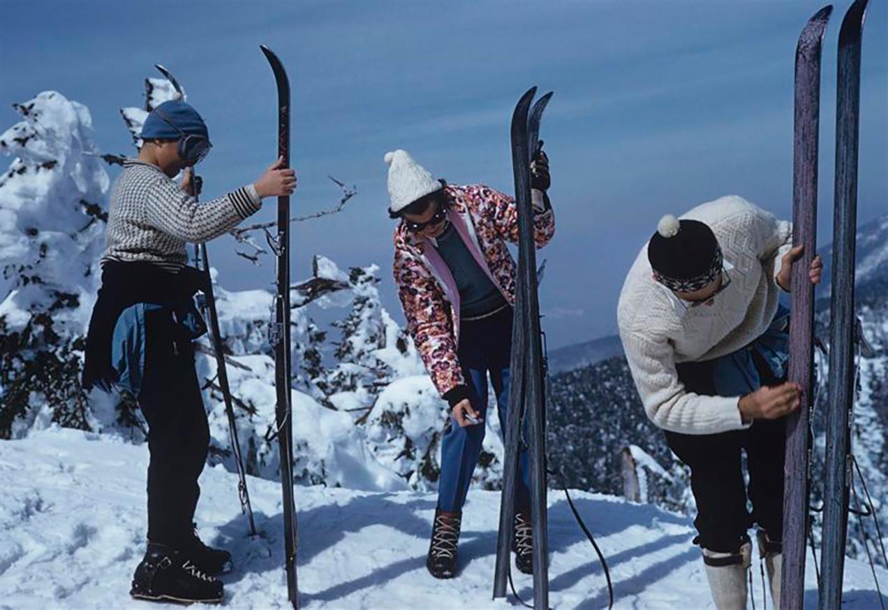Slim Aarons - On The Slopes Of Sugarbush - Nachlassgestempelte Ausgabe 
Begrenzt auf 150 Exemplare 
Drei Skifahrer inspizieren ihre Skier auf den Pisten des Sugarbush Mountain Skigebiets in Warren, Vermont, USA, um 1960. Das Sugarbush-Resort ist