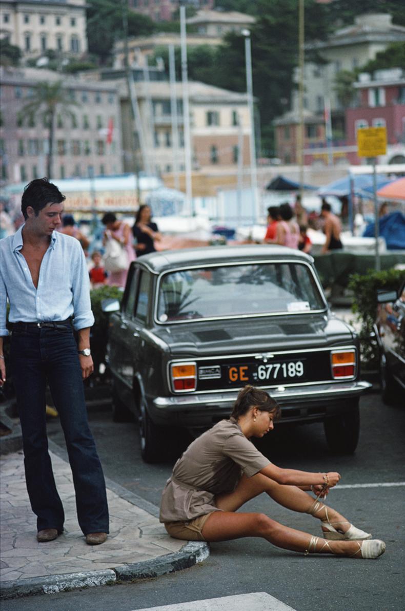 Slim Aarons - Estate Stamped Edition 
Limited to 150 only 

A man stops to watch a young woman tie her sandals on the pavement in Portofino marina, August 1977. 

(Photo by Slim Aarons). 


This photograph epitomises the travel style and glamour of