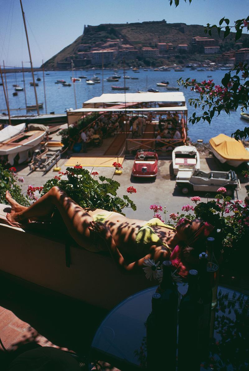Edizione con francobolli della tenuta Slim Aarons 
Limitato a 150 persone 

Una donna prende il sole su un balcone che si affaccia sul porto di Porto Ercole, Toscana, Italia, agosto 1969 (Foto di Slim Aarons)

Questa fotografia incarna lo stile di