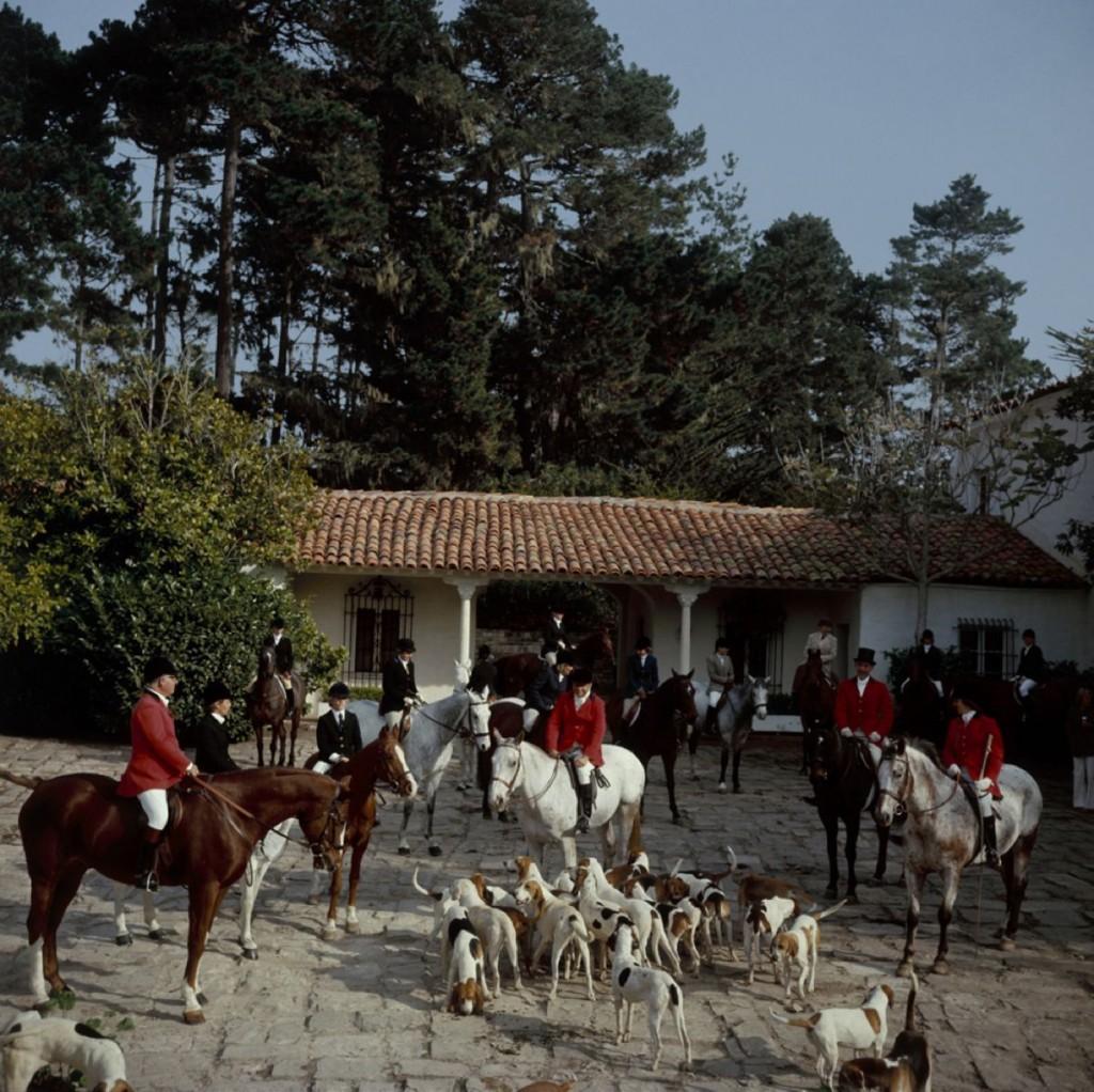 Slim Aarons Estate Print - Pebble Beach Hunt

Riders gather in the courtyard of Richard Collins’ House for the stirrup cup libation, before the start of the Pebble Beach Hunt of English and American foxhounds, November 1976. The four red-coated