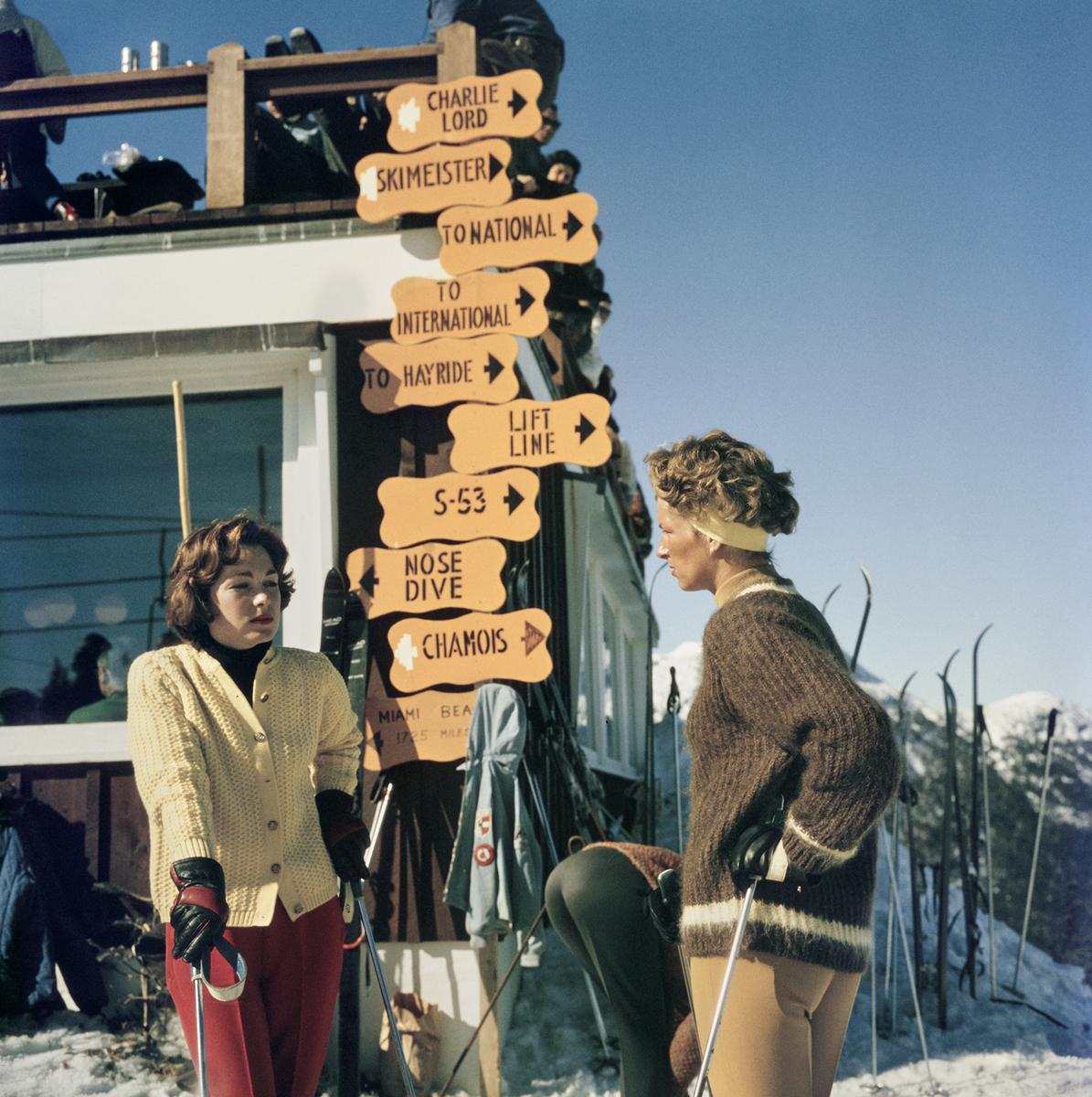 Slim Aarons Estate Print  - Skiing In Stowe


Two women in knitwear, leaning on ski sticks, while standing in the Stowe Mountain ski resort in Stowe, Vermont, 1962. Behind the two women is a sign board offering directions to the resort's