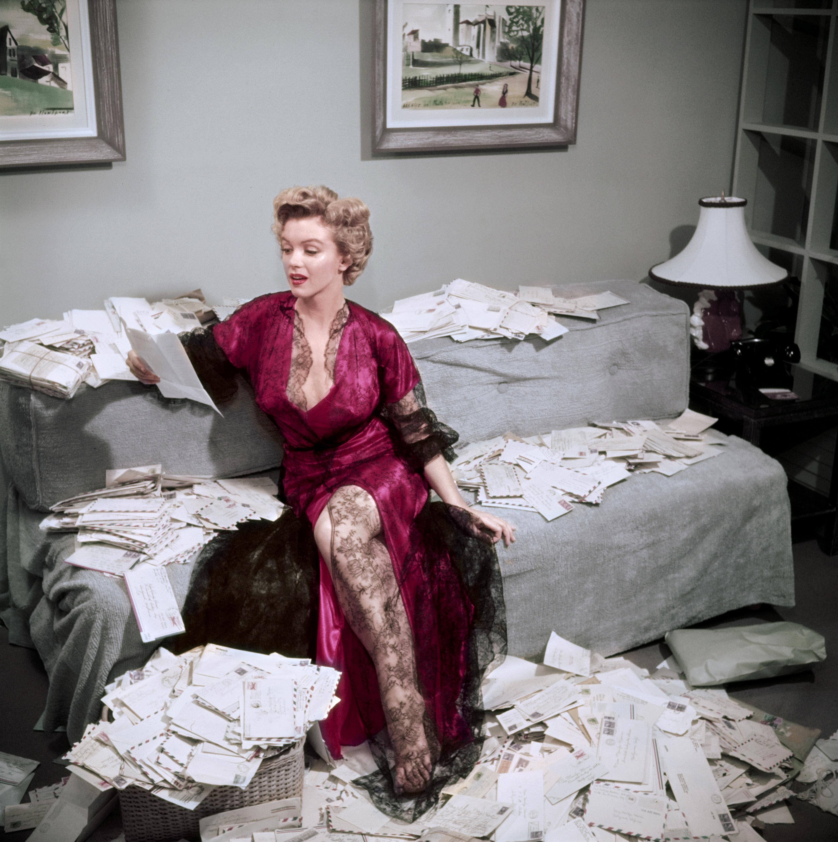Marilyn Monroe (1926 - 1962), con un picardías rojo ribeteado de encaje negro, ordena el correo de sus admiradores poco después del estreno de su película "La jungla de asfalto", Beverly Hills, 1952. (Foto de Slim Aarons/Getty Images)

Slim