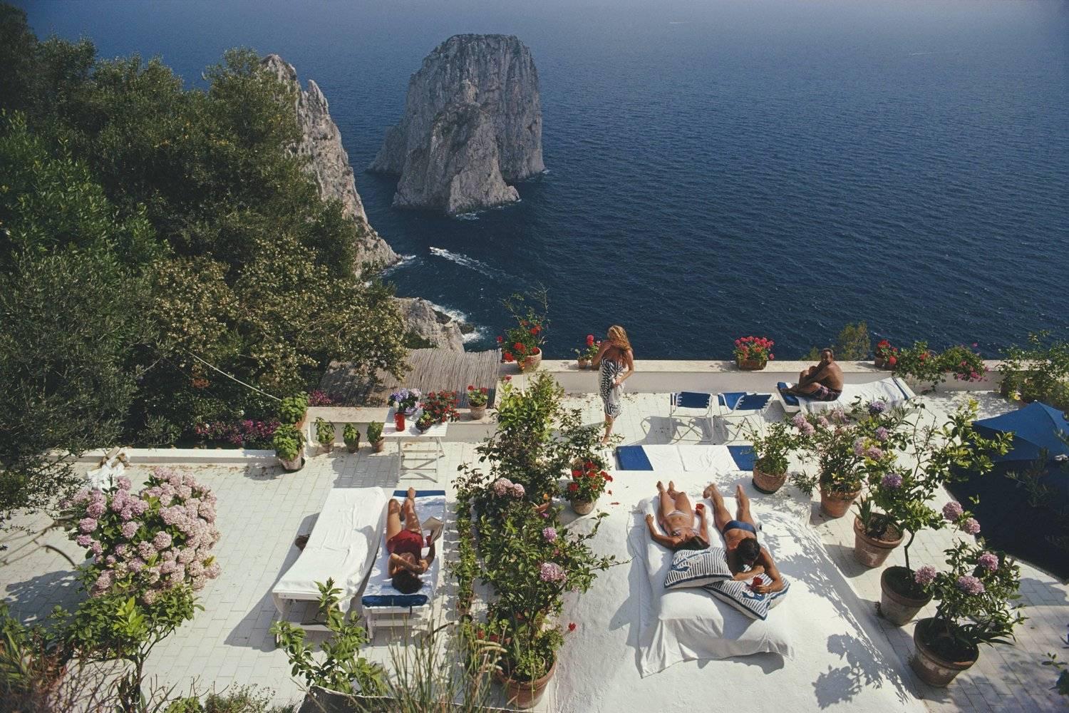Sonnenanbeter liegen im August 1980 auf der weiß gestrichenen Terrasse des Il Canille, das in die Felsen des Pizzolungo hineingebaut wurde und die Gewässer vor der Küste der Insel Capri, Italien, überblickt. Il Canille ist die Villa des