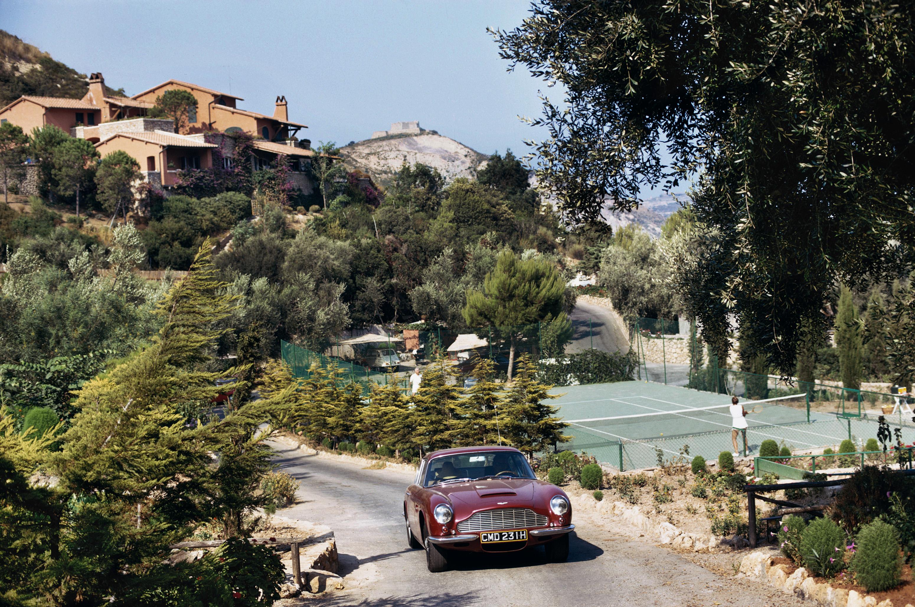 Il Pellicano Tennis
1955 (stampato successivamente)
Stampa C
Edizione stampata e numerata a mano di 150 esemplari con certificato di autenticità dell'azienda. 

Un'auto sportiva Aston Martin DB6 passa davanti ai campi da tennis dell'Hotel Il