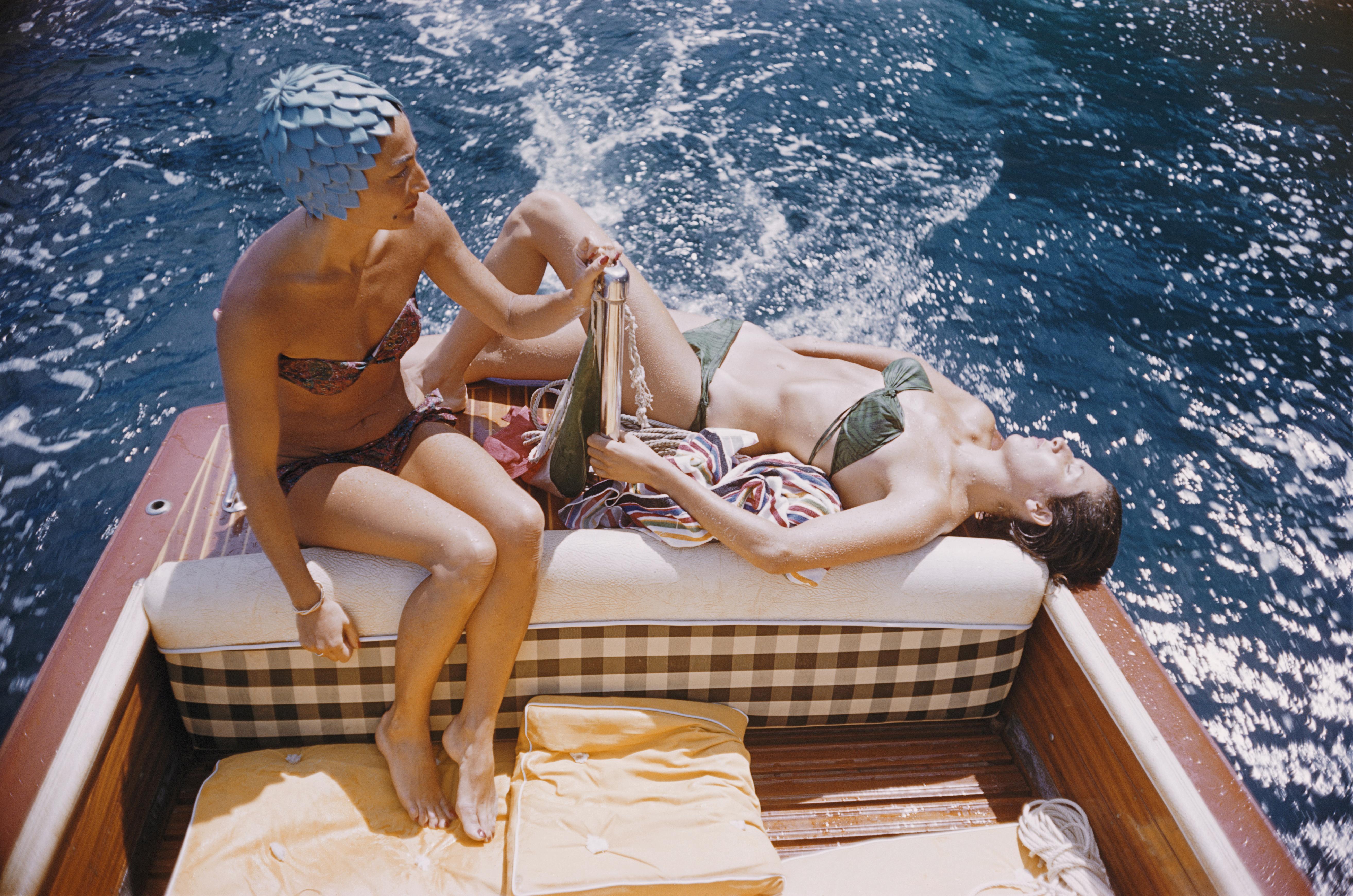 Carla Vuccino, portant un bonnet de bain, et Marina Ravas, prenant un bain de soleil, toutes deux en bikini, assises à l'arrière d'un bateau, au large de l'île de Capri, Italie, 1958.

Slim Aarons
La Dolce Vita : Vuccino et Ravas
Capri,