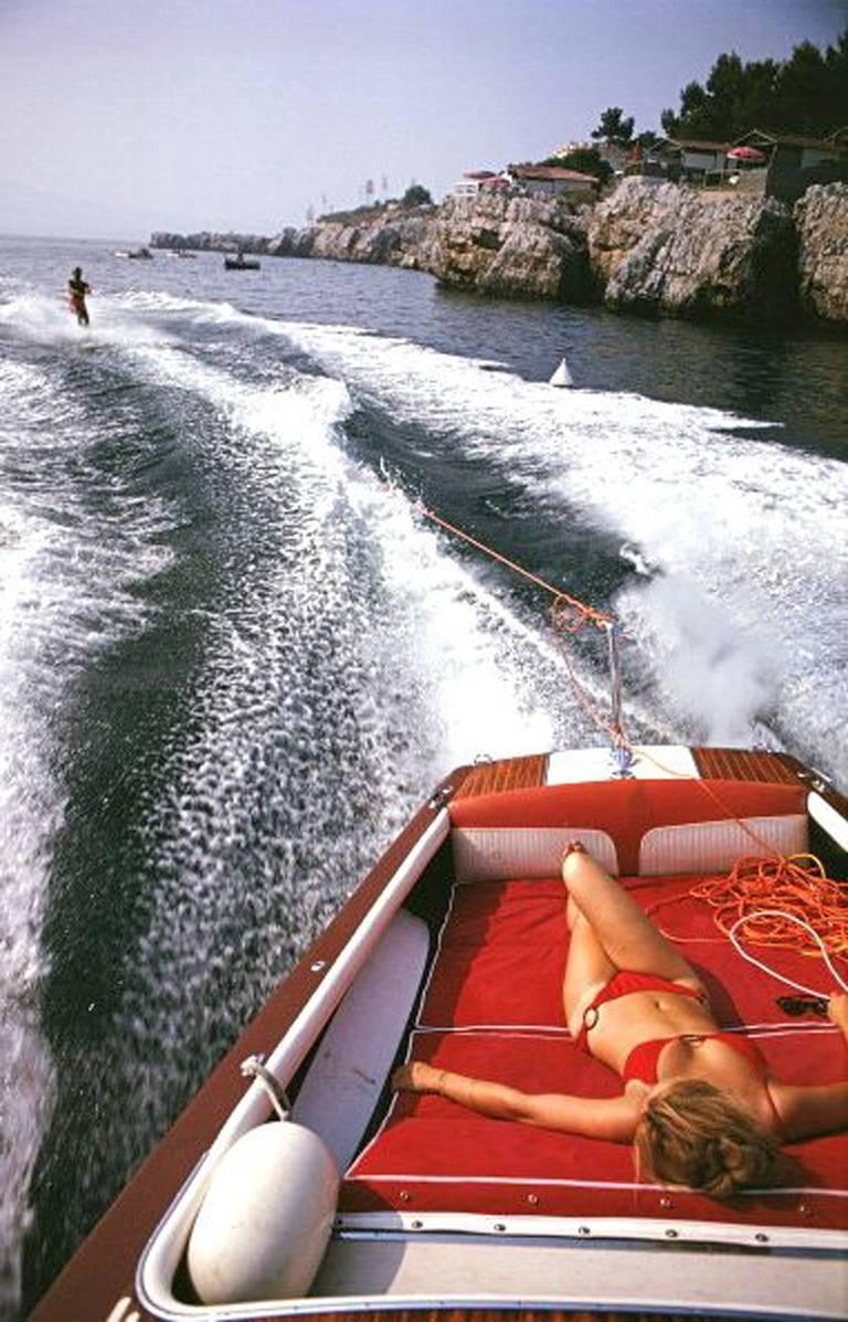 A woman sunbathing in a motorboat as it tows a waterskiier, in the sea off the Hotel du Cap Eden-Roc in Antibes on the French Riviera, August 1969.

Leisure in Antibes
Hotel du Cap Eden-Roc, French Riviera
Chromogenic Lambda print
Printed Later
Slim