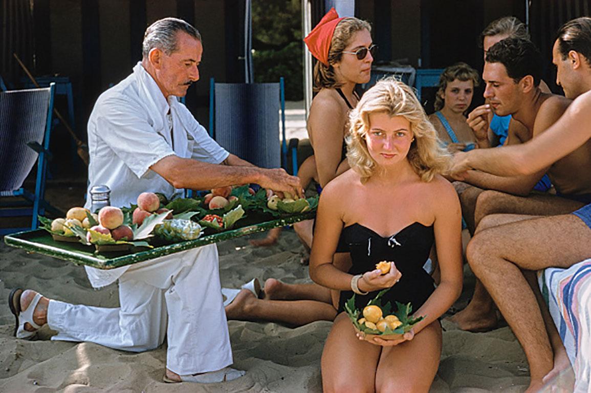 Lido Life, Venice
1957
C print
Estate stamped and hand numbered edition of 150 with certificate of authenticity from the estate.   

A waiter serves fruit to bathers, including socialite, Louisa del Musso (kneeling), at the Lido in Venice, Italy,