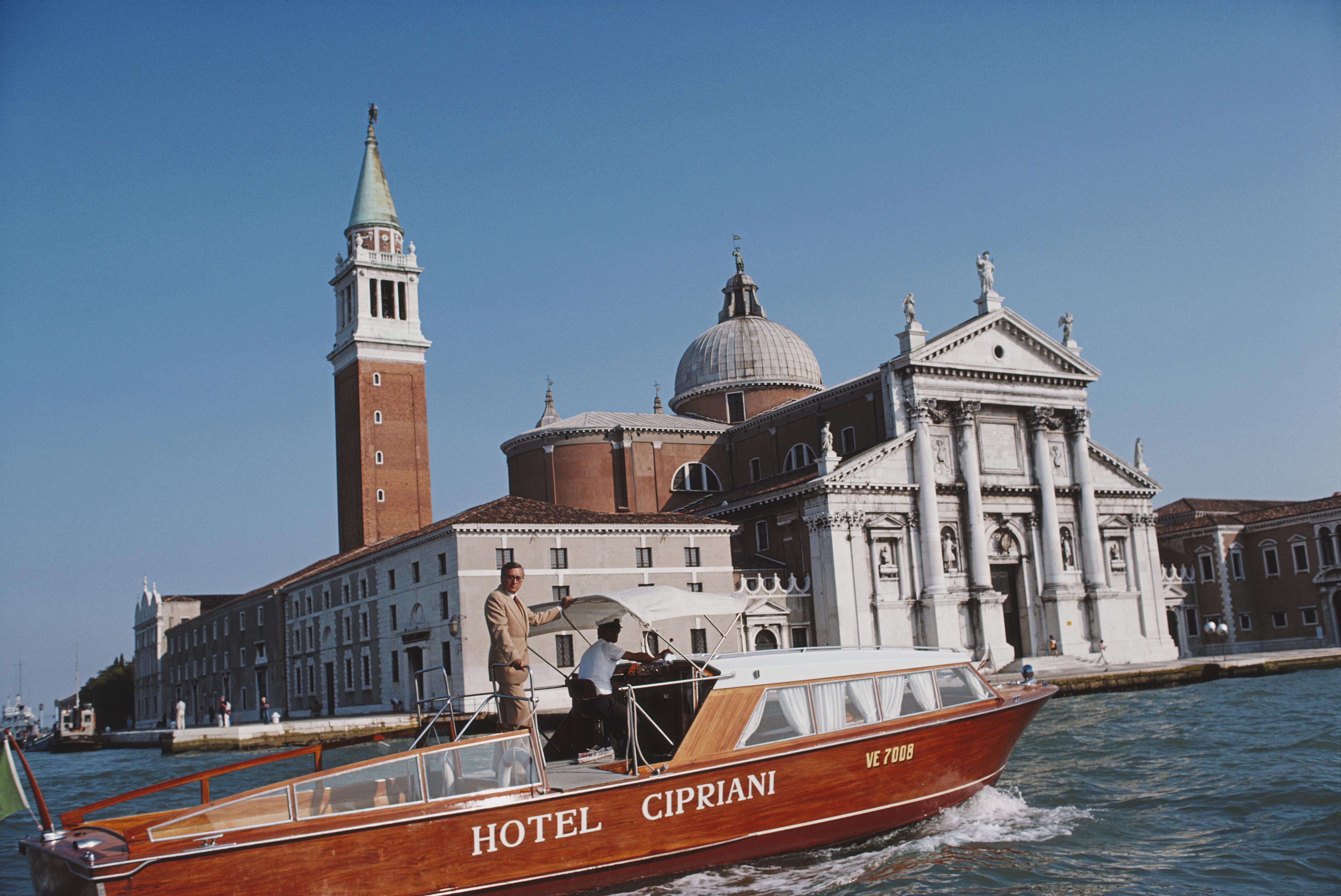 Slim Aarons
Natale Rusconi in Venice
1978 (printed later)
C print 
Estate stamped and numbered edition of 150 
with Certificate of authenticity

Natale Rusconi riding a Hotel Cipriani motor launch with the Church of San Giorgio Maggiore on San