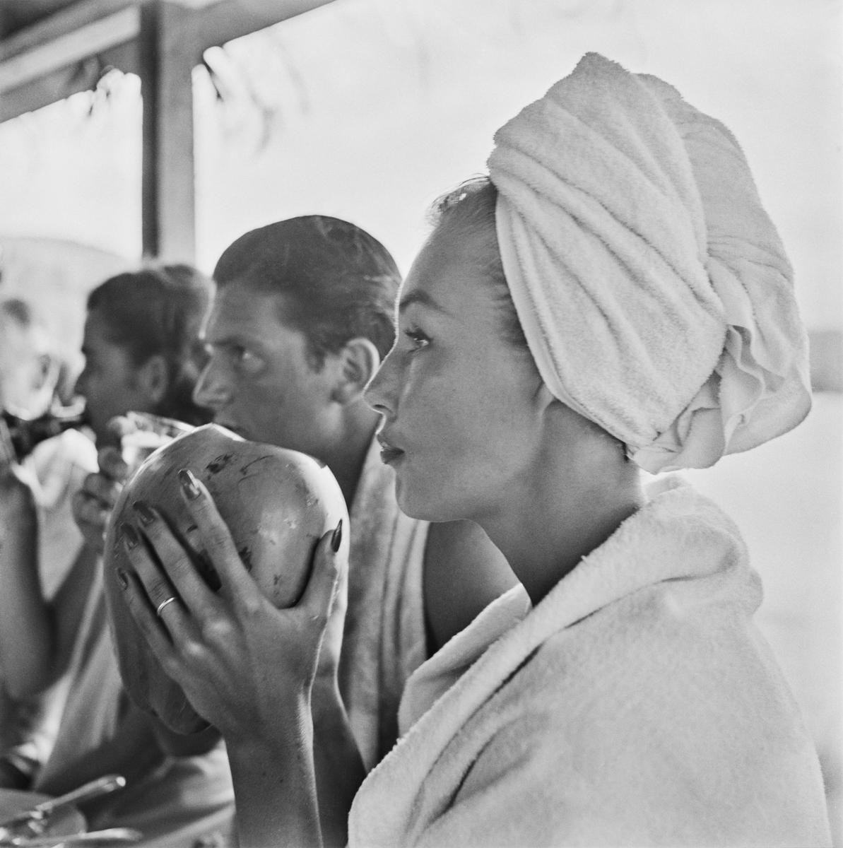 Fotomodell Liz Pringle beim Trinken aus einer Kokosnuss im Round Hill Resort, Montego Bay, Jamaika, 1953. 
Foto von Slim Aarons 

Schlanker Aarons-Silbergelatine-Druck auf Faserbasis 
Später gedruckt 
Slim Aarons Estate Edition 
Hergestellt unter