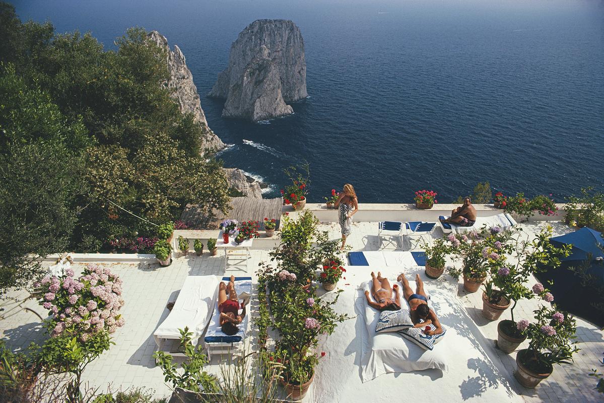 Slim Aarons Estate Print  - Il Canille 

Sunbathers lounge on the white-painted terrace of Il Canille, built into the rocks of Pizzolungo overlooking the waters off the coast of the island of Capri, Italy, in August 1980. Il Canille is the villa