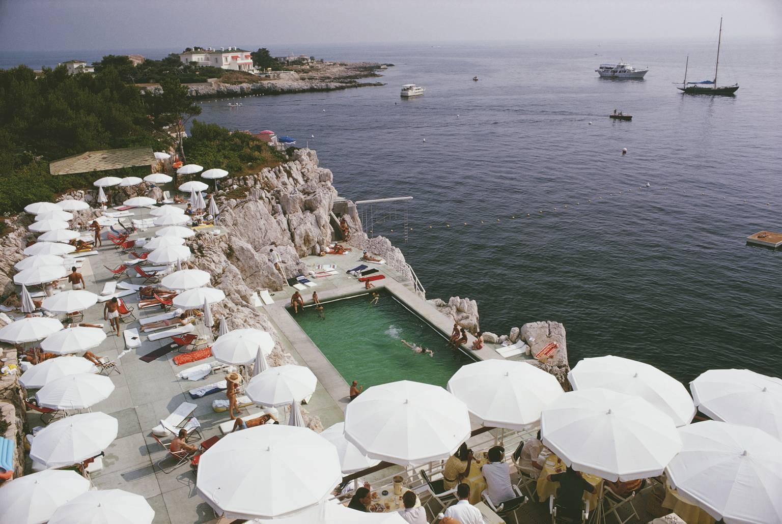 Piscina junto al mar de Slim Aarons 1969

Huéspedes y sombrillas / parasoles blancos alrededor de la piscina del infamemente glamuroso Hotel du Cap Eden-Roc, Antibes, Francia, agosto de 1969 junto al mar. 

48 x 72 pulgadas /  122 x 182 cm Tamaño