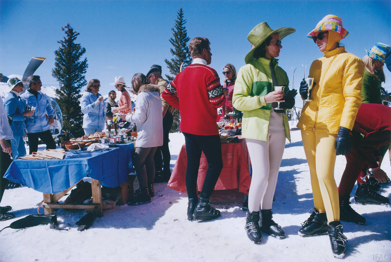 Two women, wearing brightly-coloured skiwear, stand in the foreground of a group of people attending a outdoor cocktail party in Snowmass Village, in Pitkin County, Colorado, in April 1968. 

Estate stamped and hand numbered edition of 150 with