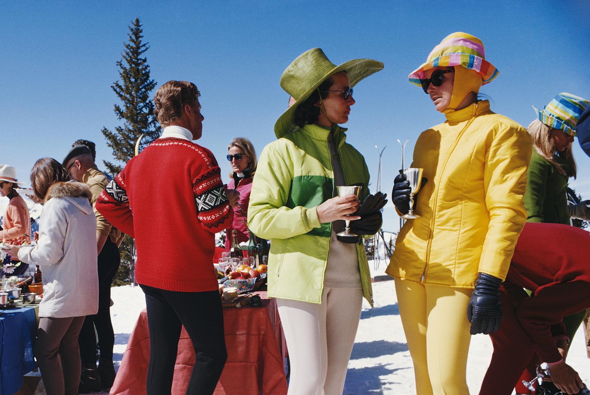 Deux femmes, portant des vêtements de ski aux couleurs vives, se tiennent au premier plan d'un groupe de personnes participant à une fête à Snowmass Village, dans le comté de Pitkin, Colorado, en avril 1968. 

Slim Aarons
Rassemblement de