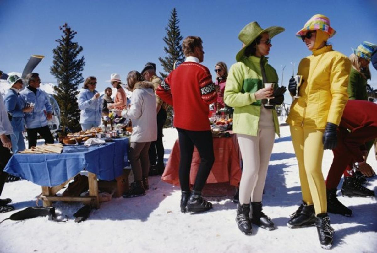 Snowmass Gathering 
1968
by Slim Aarons

Slim Aarons Limited Estate Edition

Two women, wearing brightly-coloured skiwear, stand in the foreground of a group of people attending a party in Snowmass Village, in Pitkin County, Colorado, in April