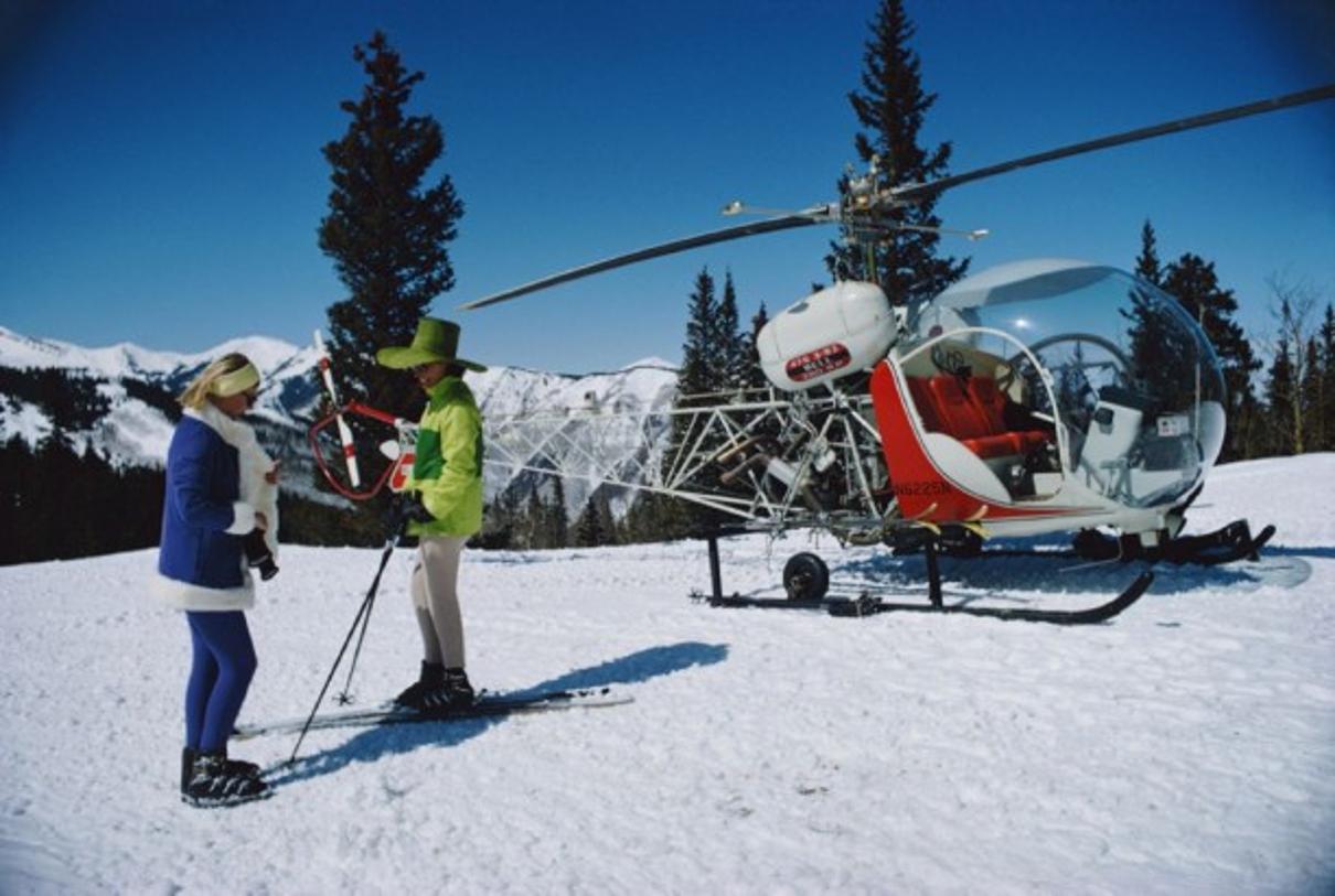 Snowmass Village 
1968
by Slim Aarons

Slim Aarons Limited Estate Edition

two fashionably attired women stand in the foreground of a snowy landscape with a helicopter on the slopes of Snowmass Village, in Pitkin County, Colorado, in March