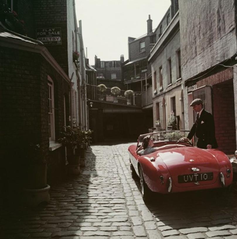 Sports Car Couple 
1955
by Slim Aarons

Slim Aarons Limited Estate Edition

John Bryant with his AC sports car in Kinnerton Place, London SW1. His passenger is Margaret McAulay. Circa 1955

unframed
c type print
printed 2023
16×16 inches - paper