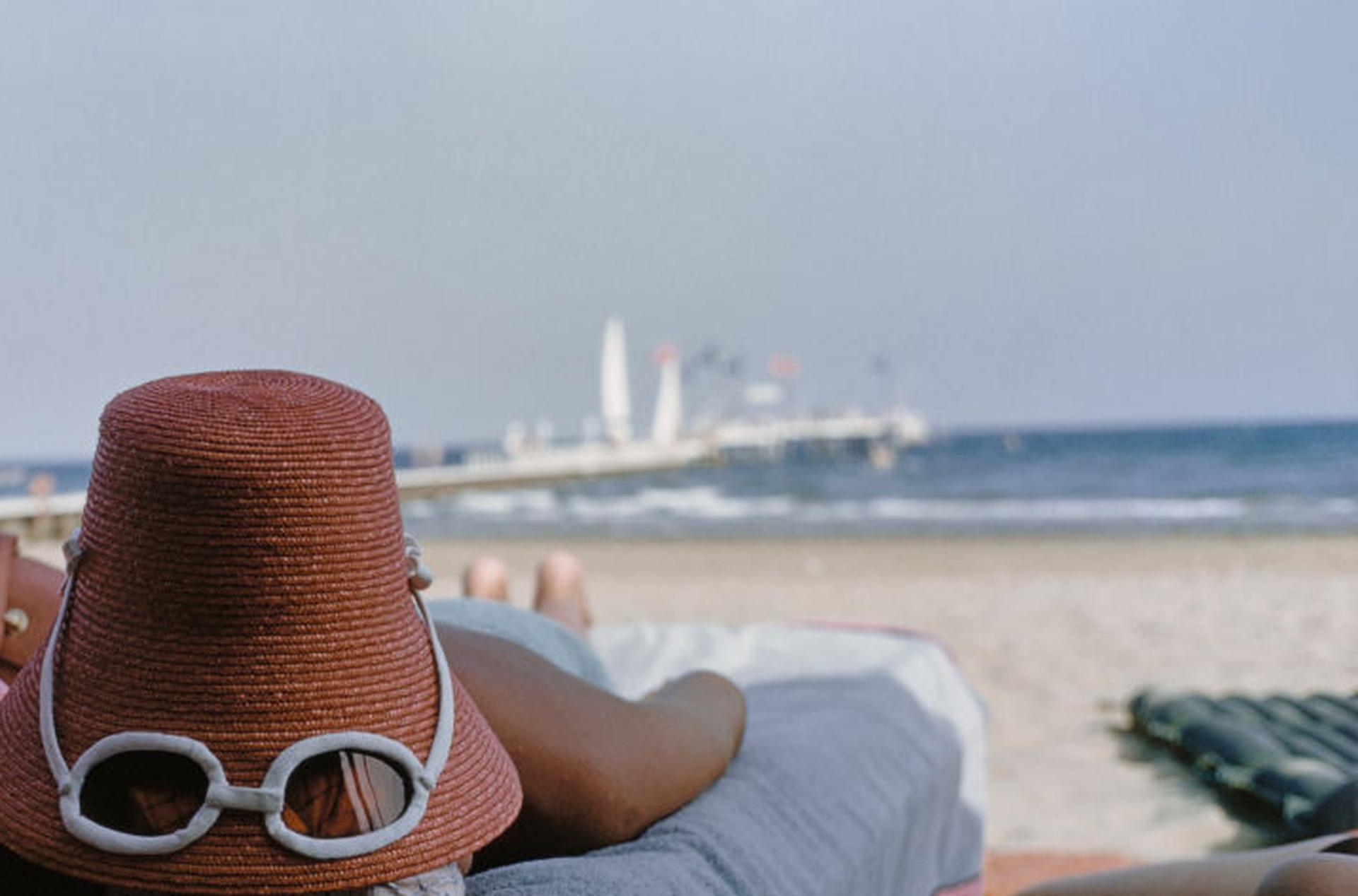 Dieses Porträtfoto des Gesellschaftsfotografen Slim Aarons aus der Mitte der 1950er Jahre zeigt einen  Frau beim Sonnenbaden, mit neuartigem Sonnenhut aus Stroh mit integrierter Sonnenbrille, Venedig.

Dies ist eine nachlassgestempelte und