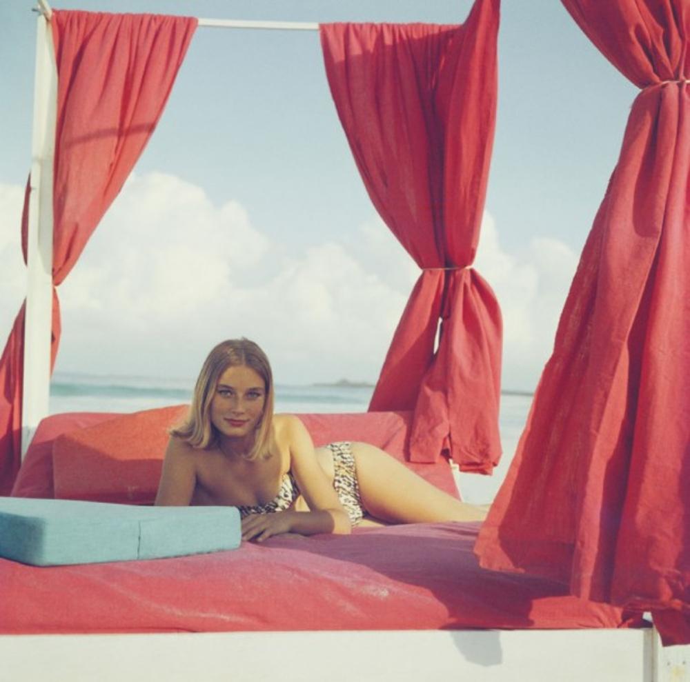Tania Mallet 
1961
by Slim Aarons

Slim Aarons Limited Estate Edition

1961: Actress Tania Mallet relaxes on a red-curtained four poster in Eleuthera, in the Bahamas. She is best known for her role as the unfortunate Tilly Masterson in the Bond film