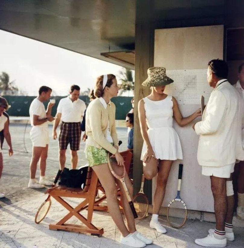 Tennis auf den Bahamas 
1957
von Slim Aarons

Slim Aarons Limited Estate Edition

Zwei Frauen unterhalten sich mit einem Mann am Rande eines Tennisplatzes auf den Bahamas, ca. 1957. Hinter der Hauptgruppe steht eine zweite Gruppe von Personen, die