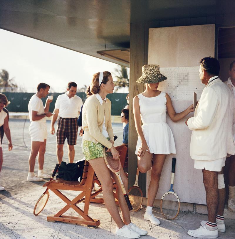 Tennis alle Bahamas' 1957

Slim Aarons Edizione Limitata Estate 
(edizione 1/150)
 
Due donne parlano con un uomo sul bordo di un campo da tennis alle Bahamas, nel 1957 circa. 
Dietro il gruppo principale c'è un secondo gruppo di persone che parla.