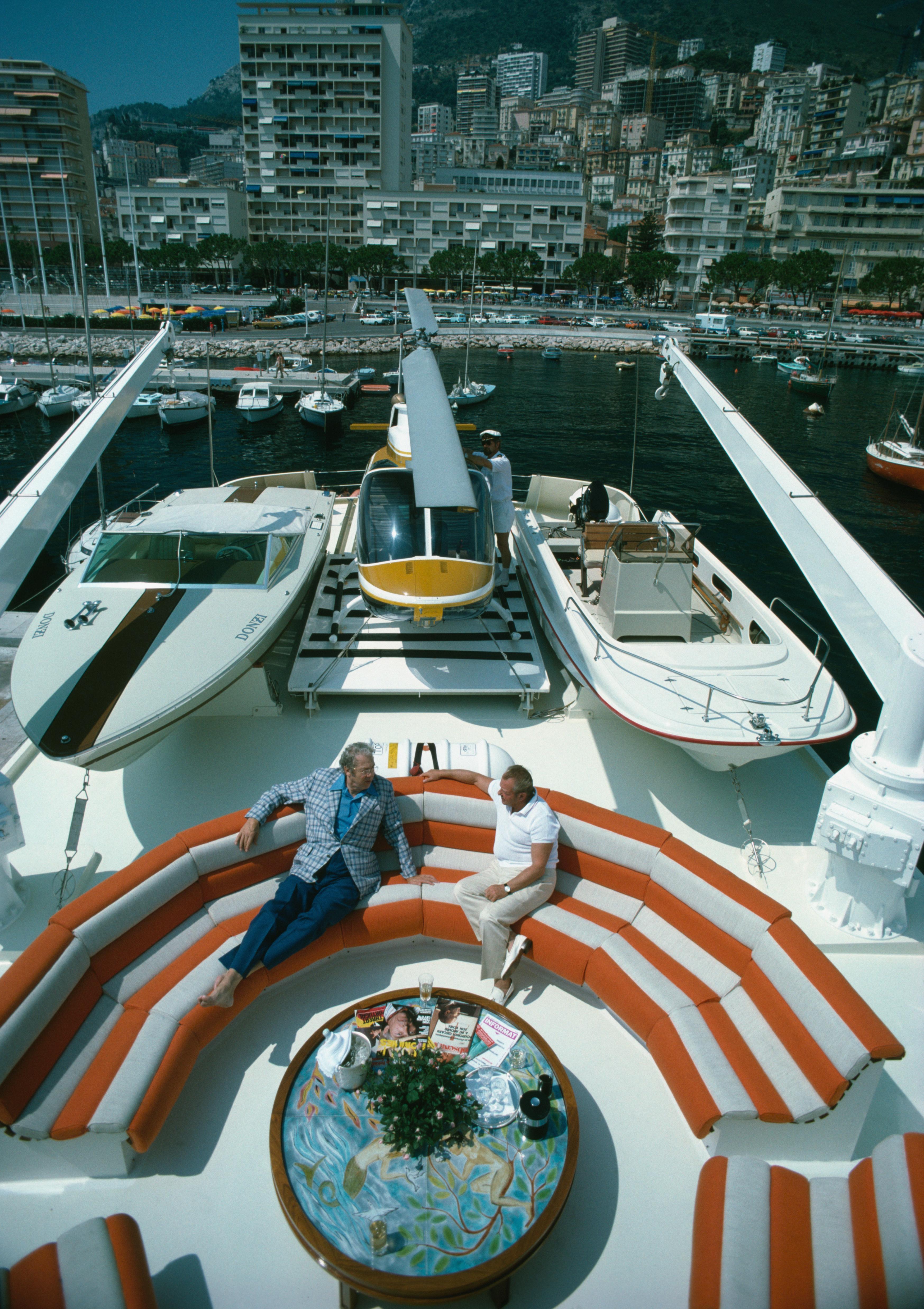 'Transport Buffs' 1981 Slim Aarons Limited Estate Edition Print 

A helicopter and two motor boats adorn the deck of a luxury yacht where Iowan businessman Roy J Carver and the Prince de Polignac are chatting in Monte Carlo harbour.

Produced from