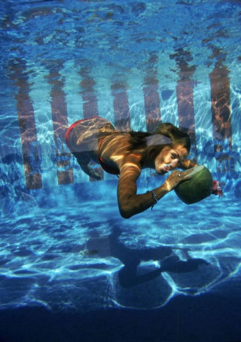 Schlanke Aarons
Unterwassergetränk, 1972
Chromogener Lambda-Druck
Nachlassgestempelte und handnummerierte Auflage von 150 Stück mit Echtheitszertifikat des Nachlasses.

Eine Frau trinkt aus einer Kokosnuss unter Wasser im Pool des Las Brisas Hotels