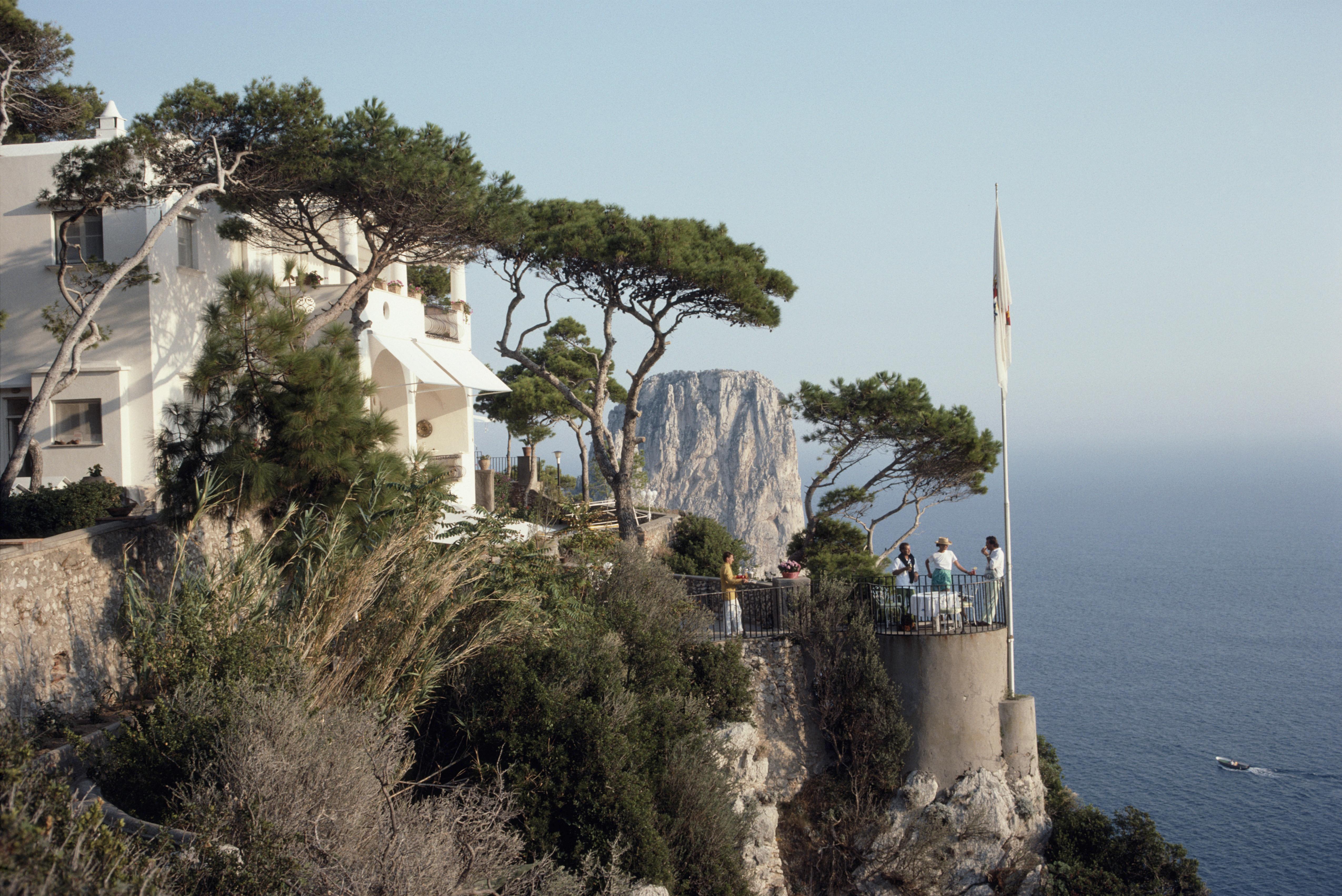 unghia Marina" 1989 Slim Aarons Edition limitée du domaine 

Un groupe de personnes se tient sur une terrasse, à la marina Unghia sur l'île de Capri, en Italie, en septembre 1989. Des arbres parsèment le côté de la marina tandis qu'un mât de drapeau