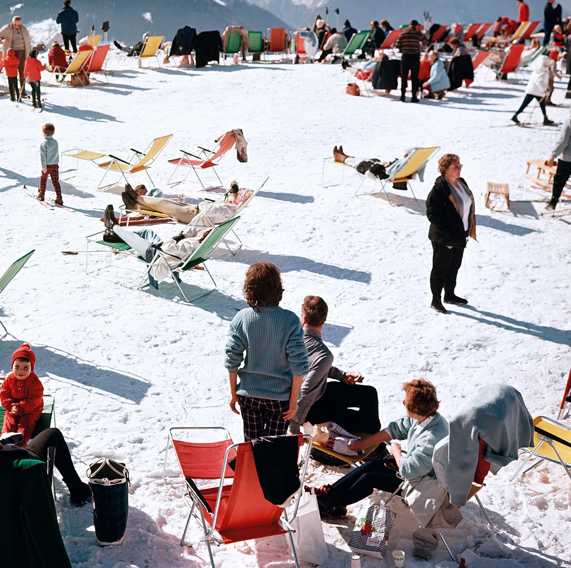 Schweizer Alpen, 1964: Diese Landschaftsaufnahme des Society-Fotografen Slim Aarons zeigt Urlauber, die den Sonnenuntergang auf einem weiß verschneiten Berggipfel in Verbier, Schweiz, im Jahr 1964 genießen.

Klassische Szene des Glamours der