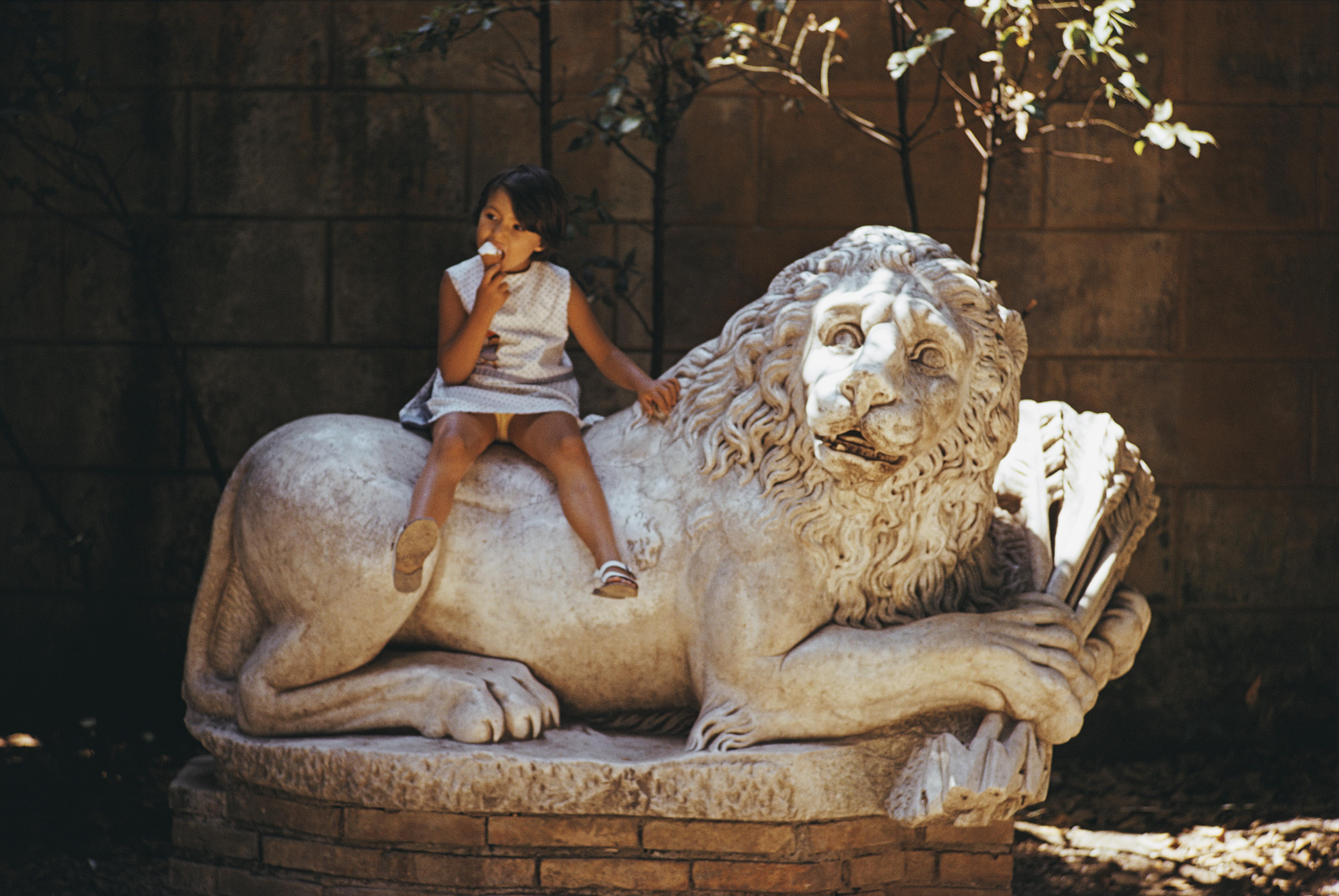 'Villa Borghese Lion' 1970 Slim Aarons Limited Estate Edition Print 

A young girl eating an ice cream while sitting on a sculpture of a lion in the grounds of the Villa Borghese in Rome, Italy, 1970. 

Produced from the original