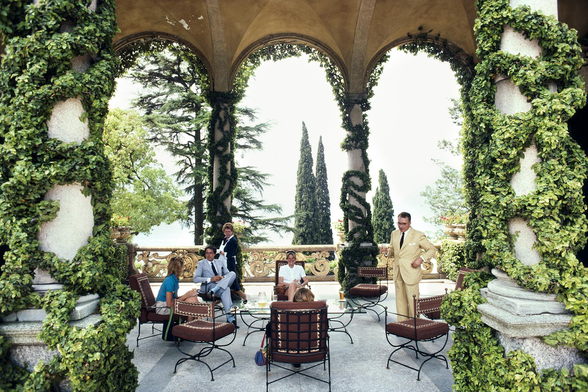 Tauchen Sie ein in den ruhigen Luxus des Comer Sees mit dieser exquisiten Fotografie von Slim Aarons, die den italienischen Bergsteiger und Entdecker Guido Monzino (1928-1988) zeigt. Sie wurde im Juni 1983 in seiner Villa del Balbianello in Lenno,