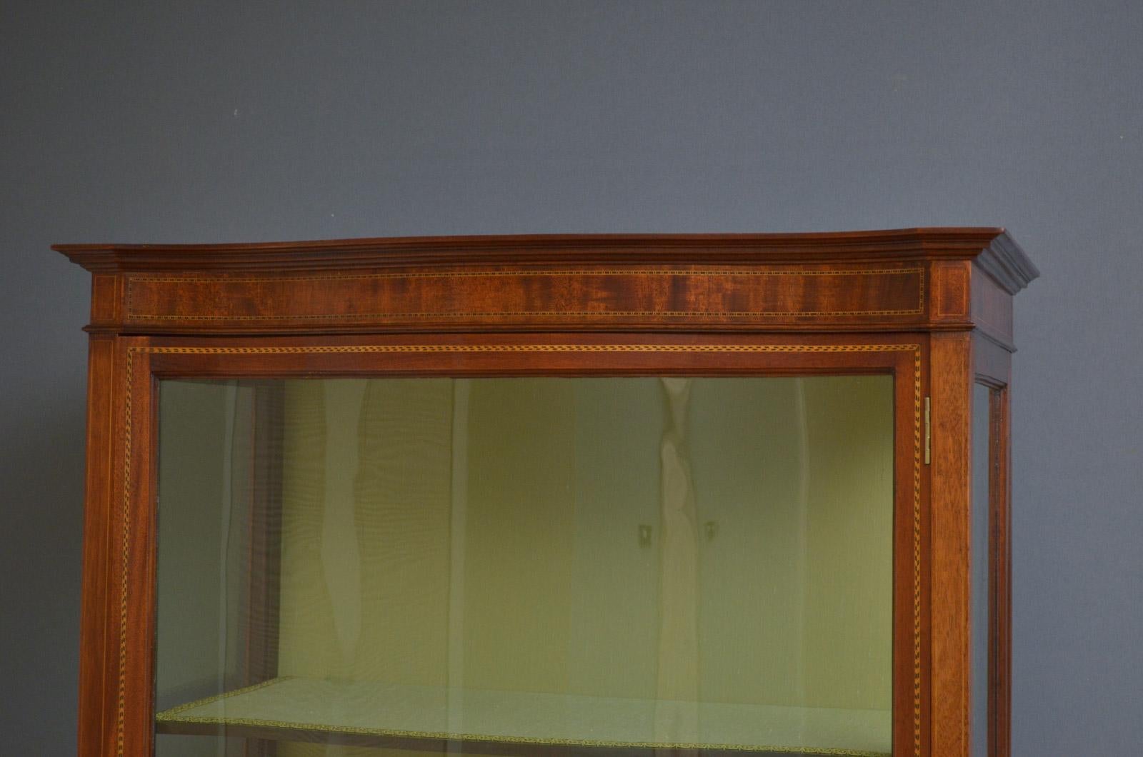 Sn4441, slim Edwardian, mahogany display cabinet, vitrine of serpentine outline, having molded cornice above a satinwood inlaid frieze, single door enclosing 3 shelves and glazed sides, all standing on elegant legs terminating in spade feet. This