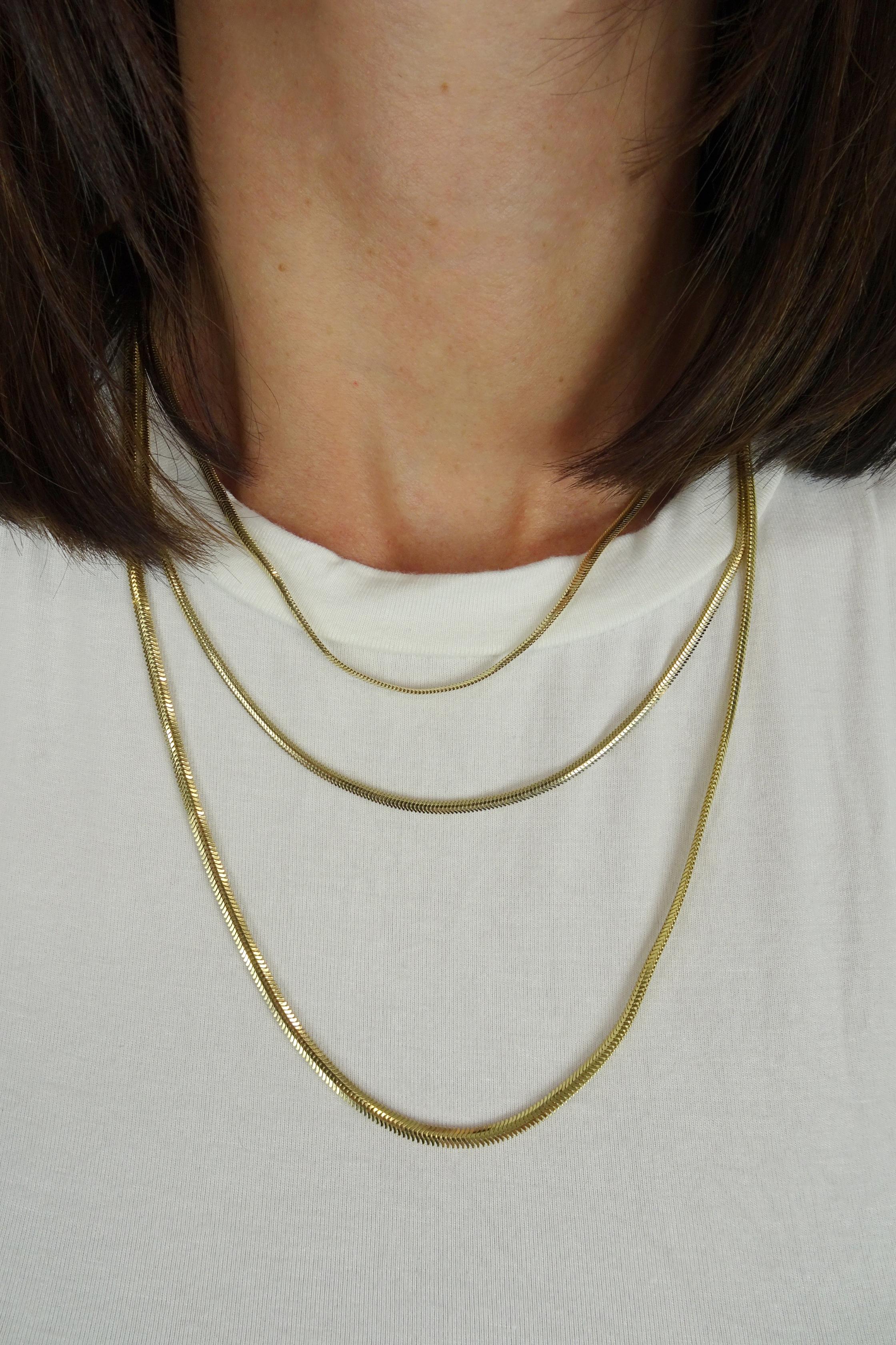 El Collar de Oro con Cadena Plana Slim es el epítome de la elegancia contemporánea y la sofisticación minimalista. Elaborado en lustroso oro de 14 quilates, este collar presenta un diseño de cadena plana y esbelta que destila sencillez con un toque