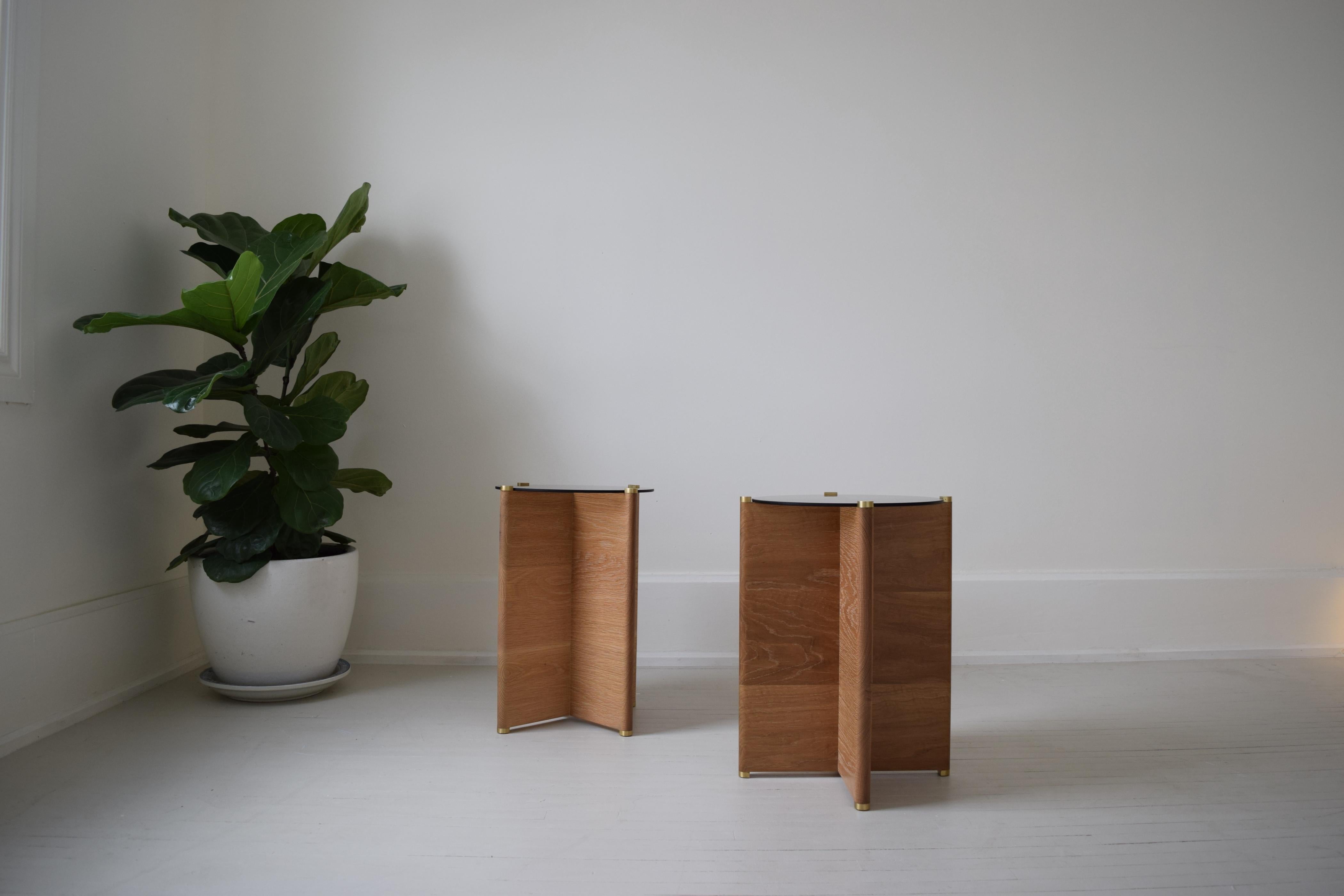 Slim Table ist ein Beistelltisch mit einem Gestell aus massiver Weißeiche und Messingdetails, das eine runde Platte aus Rauchglas trägt. Mit einem handgeriebenen Hartwachsöl veredelt. 