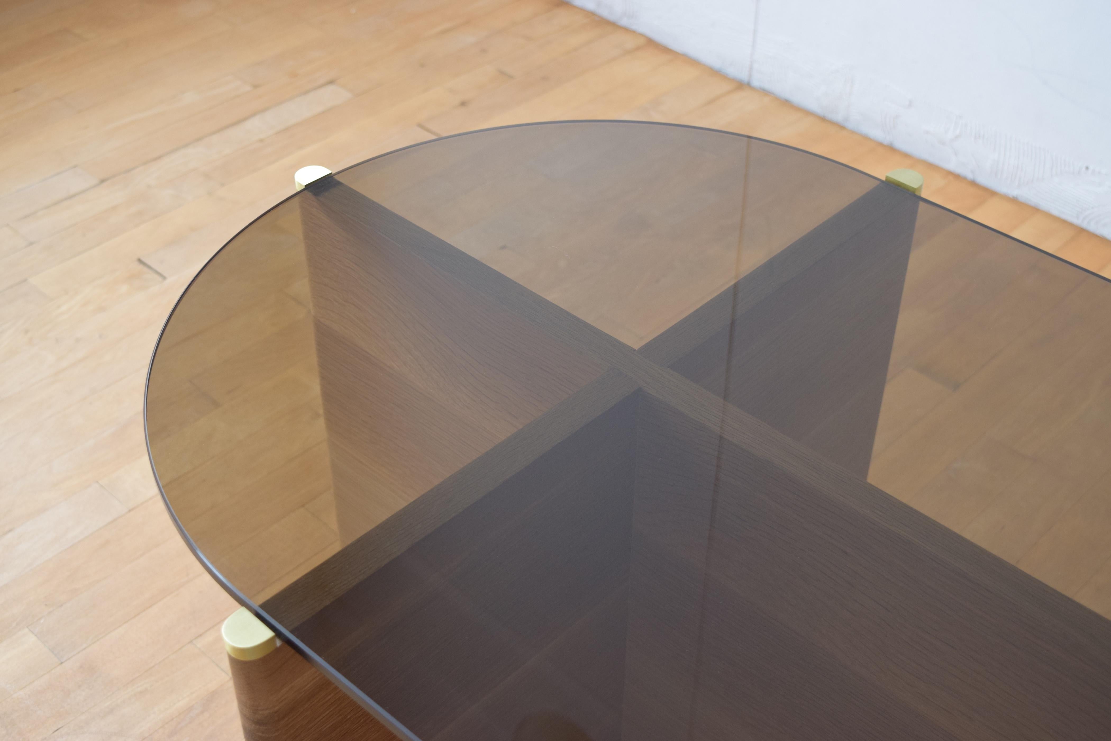 La table Slim est une table basse en bois massif et verre fumé. Le cadre est en chêne blanc rift avec des détails en laiton et supporte un plateau en verre fumé dans une forme classique de pilule.