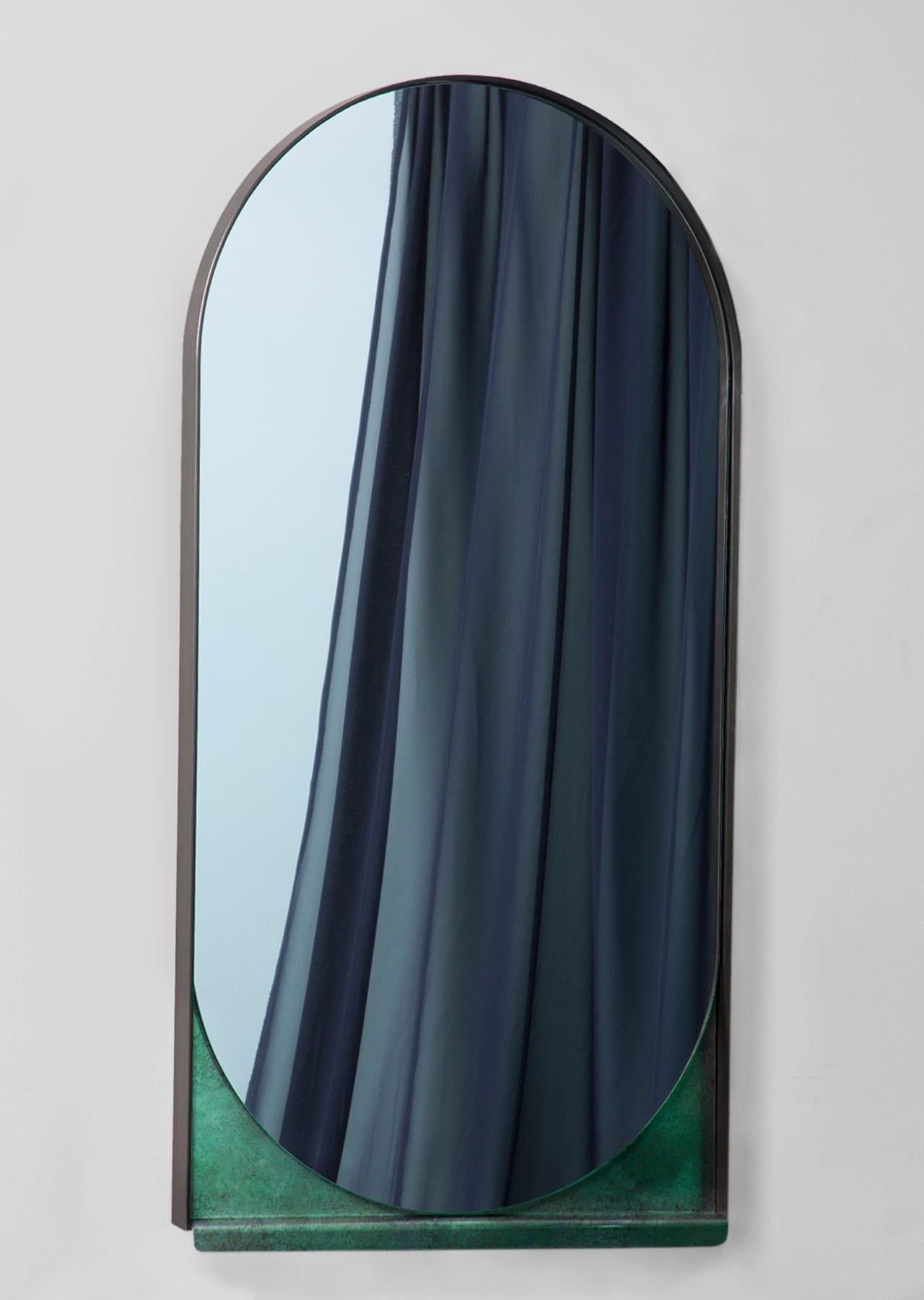 Simplicity is key to the Slip Mirror, whose thin blackened stainless steel frame delicately holds an oblong mirror. A contrasting verdigris shelf slips out from below, hinting at hidden layers beneath.
 