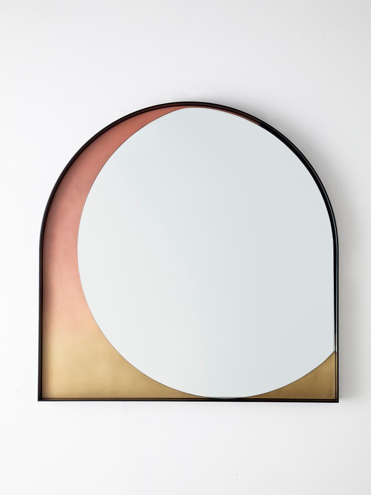 Simplicity is key to the slip mirror, whose thin blackened stainless steel frame delicately holds the suggestion of a round mirror. A contrasting patinated bronze gradient is revealed, hinting at layers hidden beneath.
 