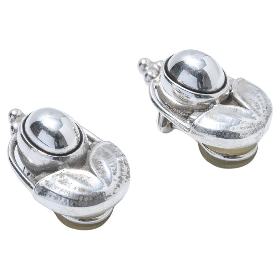 These earrings are crafted from silver, featuring a polished, spherical centerpiece that reflects light beautifully. Around the central sphere, the silver is molded into intricate, organic shapes, resembling leaves or petals, with a textured finish