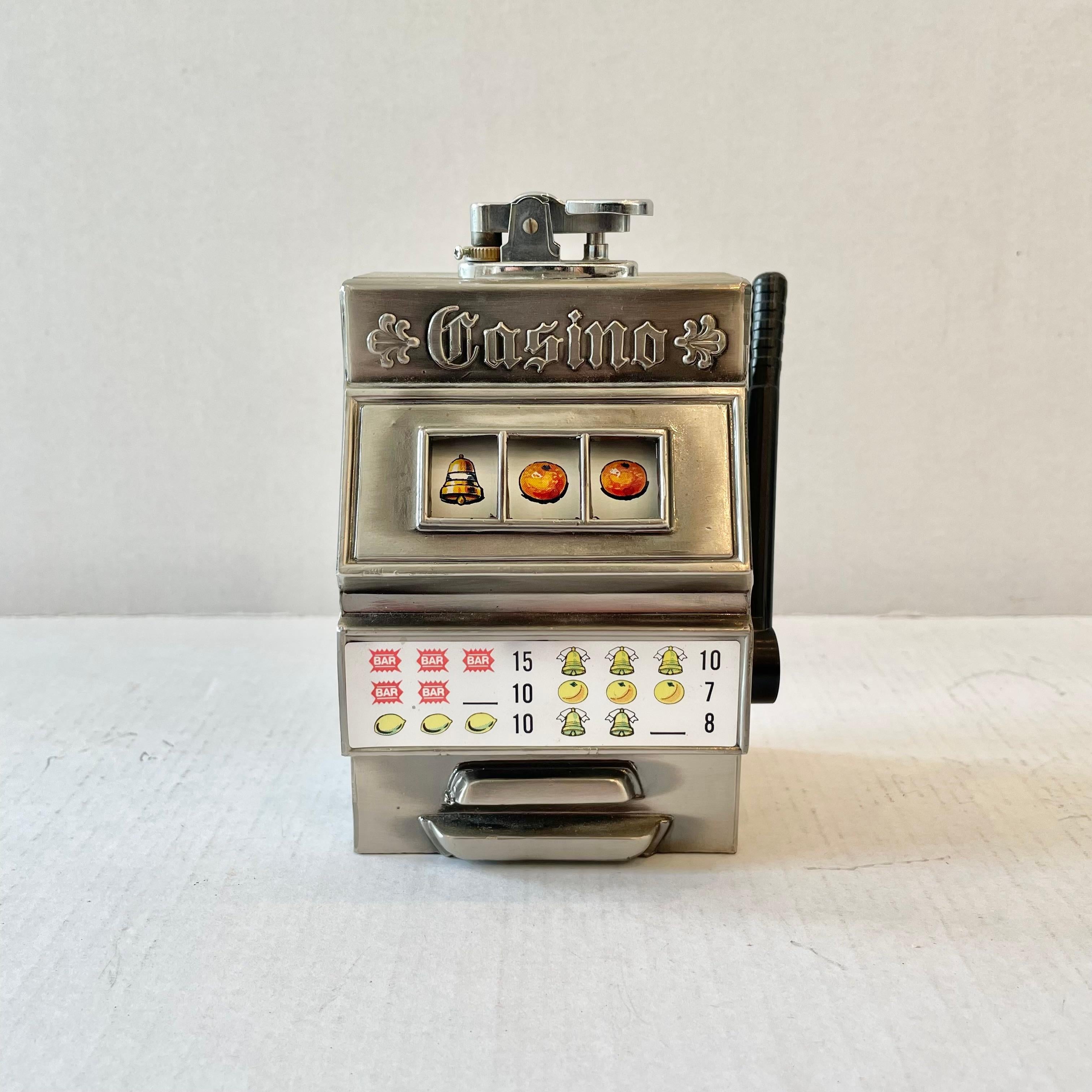 Cool 1980s table lighter in the shape of a working slot machine. Comoys of London - 'Made In Japan' sticker on the underside. This vintage piece has great balance and details like a functioning pull lever and image reel with graphics of fruits,