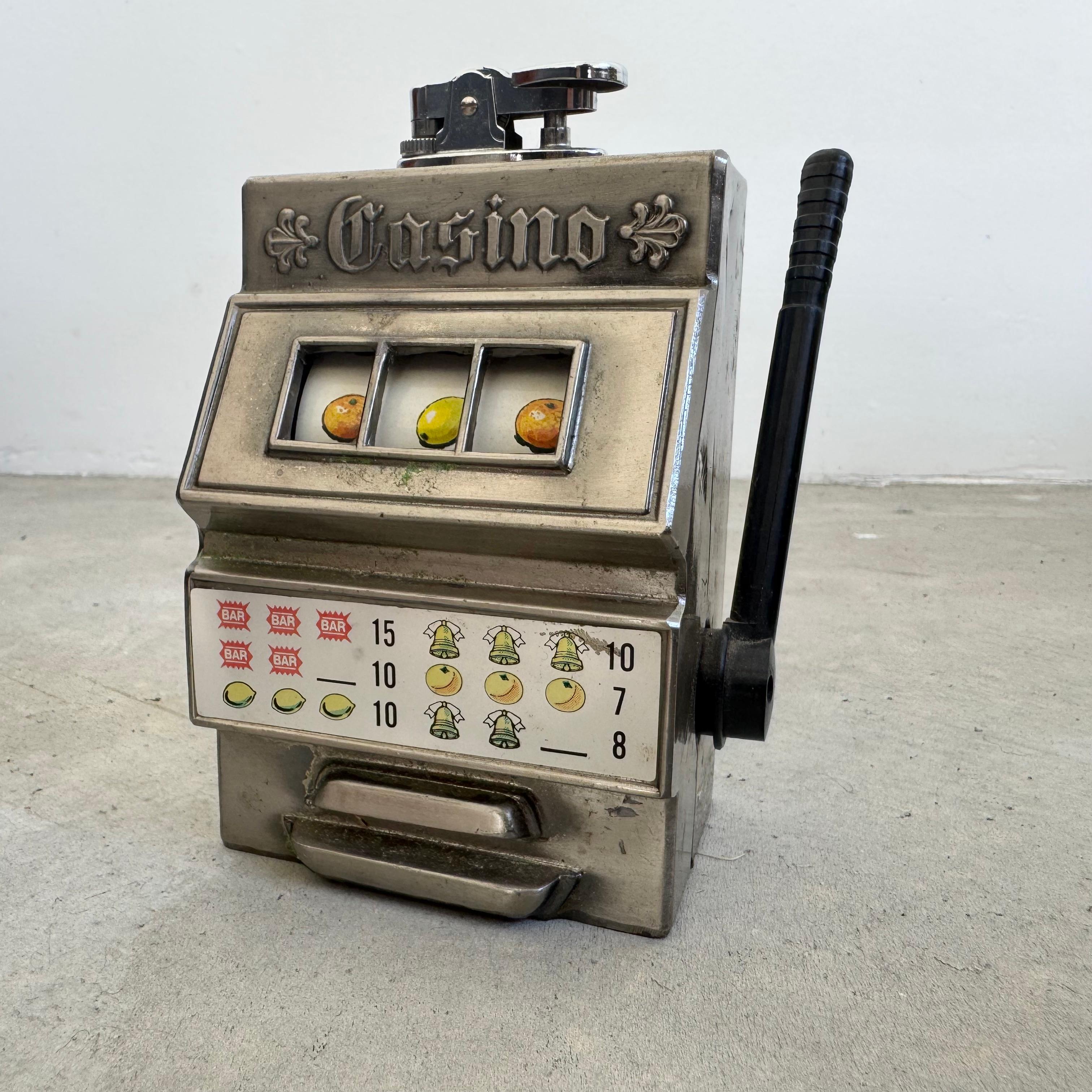 Das coolste kleine Tischfeuerzeug, gegossen in Form eines funktionierenden Spielautomaten. Dieses Vintage-Stück verfügt über sorgfältige Details mit einem funktionierenden Zughebel und einer Bildrolle mit Grafiken von Früchten, Glocken und