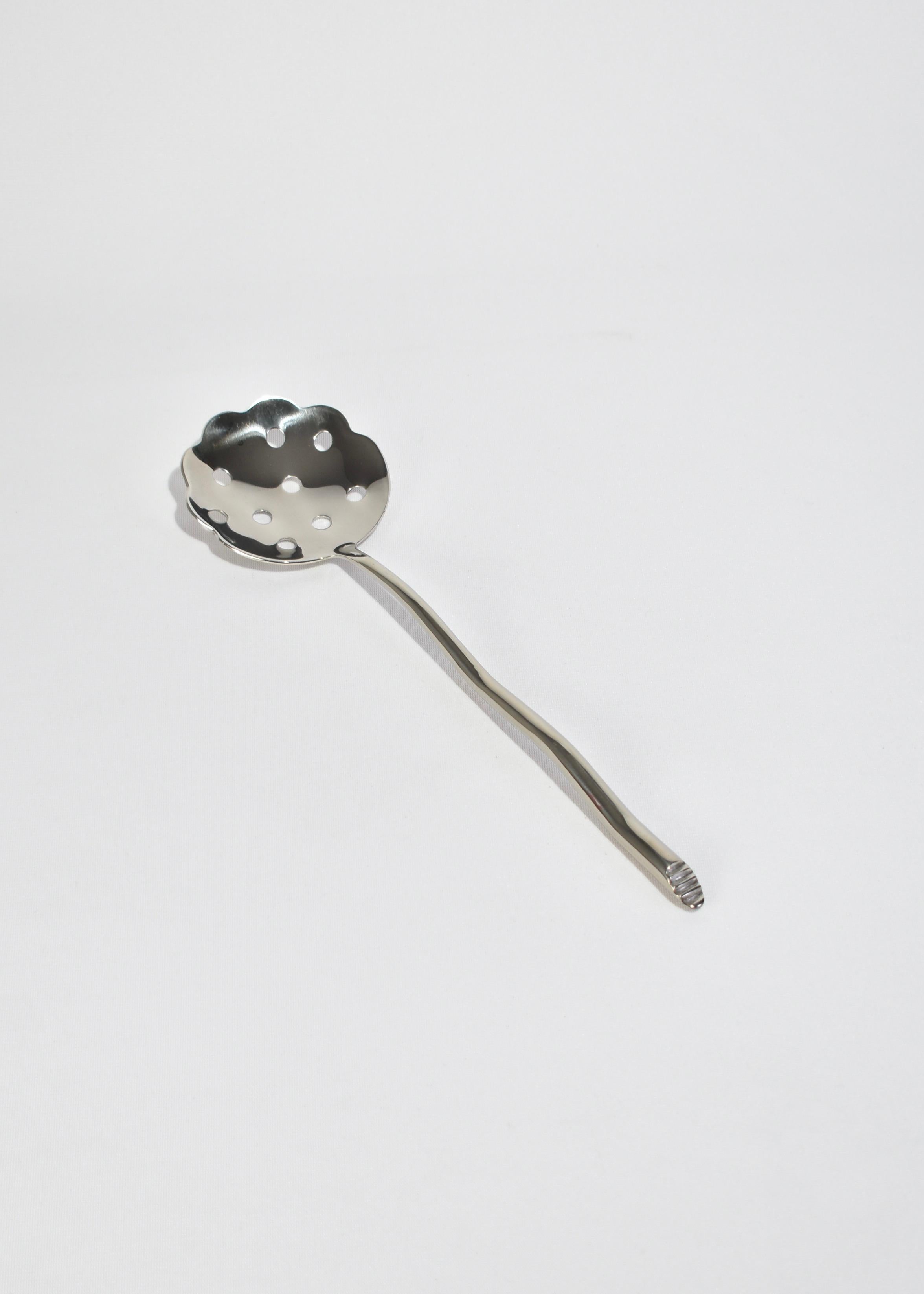 Stainless steel slotted serving spoon in 'Shore' pattern. Features an undulating handle with angled end. Impressed above knob on side of handle: 'IZABEL LAM'. 

Designed in the late 1980s by Izabel Lam, available exclusively.