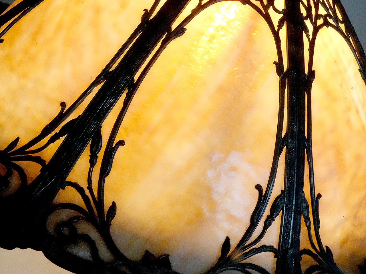 This is a nicely designed table lamp. It has a curved shade with 6 unique latticework filigree overlays. Each slump glass (curved) panel features a cream -  amber variegated glass. It is lit by one E26 bulb. All the cast metal parts have a faint