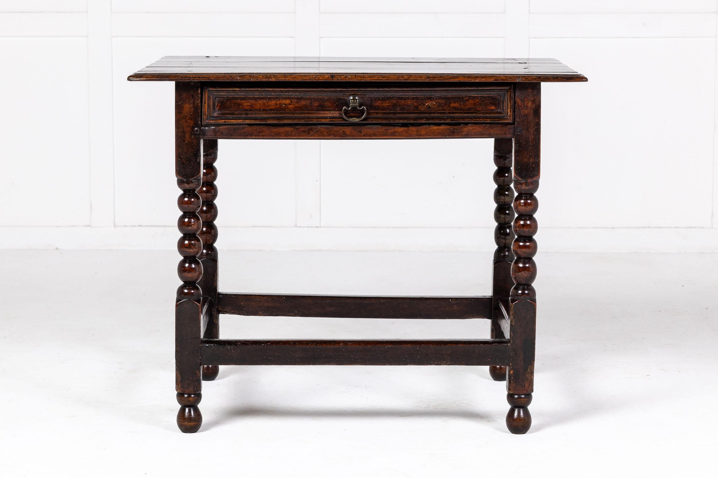 A Fine and Small 17th Century English Oak Side or Occasional Table.

The fine three planked overhanging top above a single drawer with panelled detailing, supported by square legs with bobbin turned elements. The legs joined by an H-form stretcher