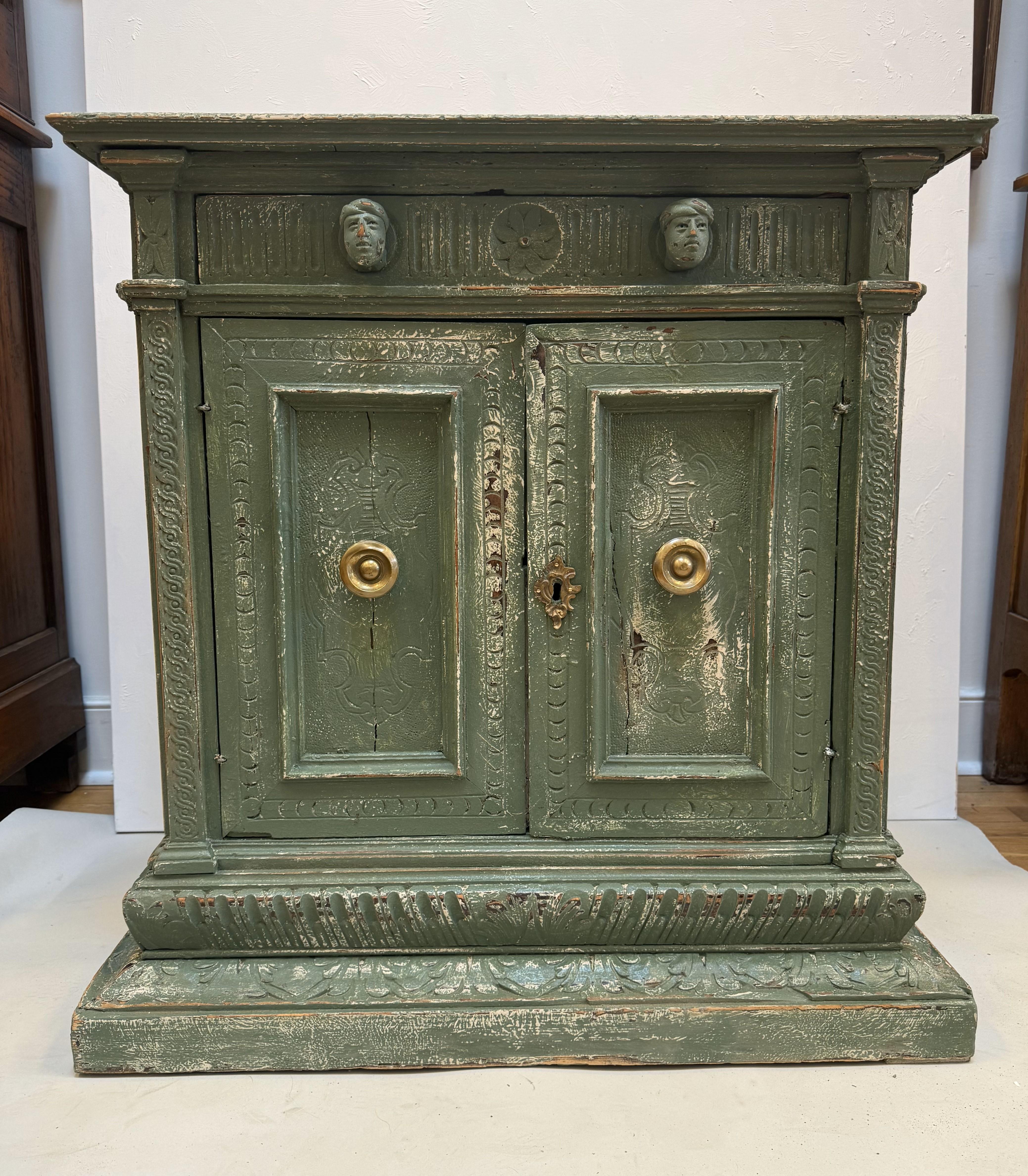 Small 17th Century Italian Renaissance Credenza. Made of Circassian Walnut with carved heads as handles to the single drawer over two paneled doors with bronze hardware and heavily carved molded decoration throughout. Retaining old green painted