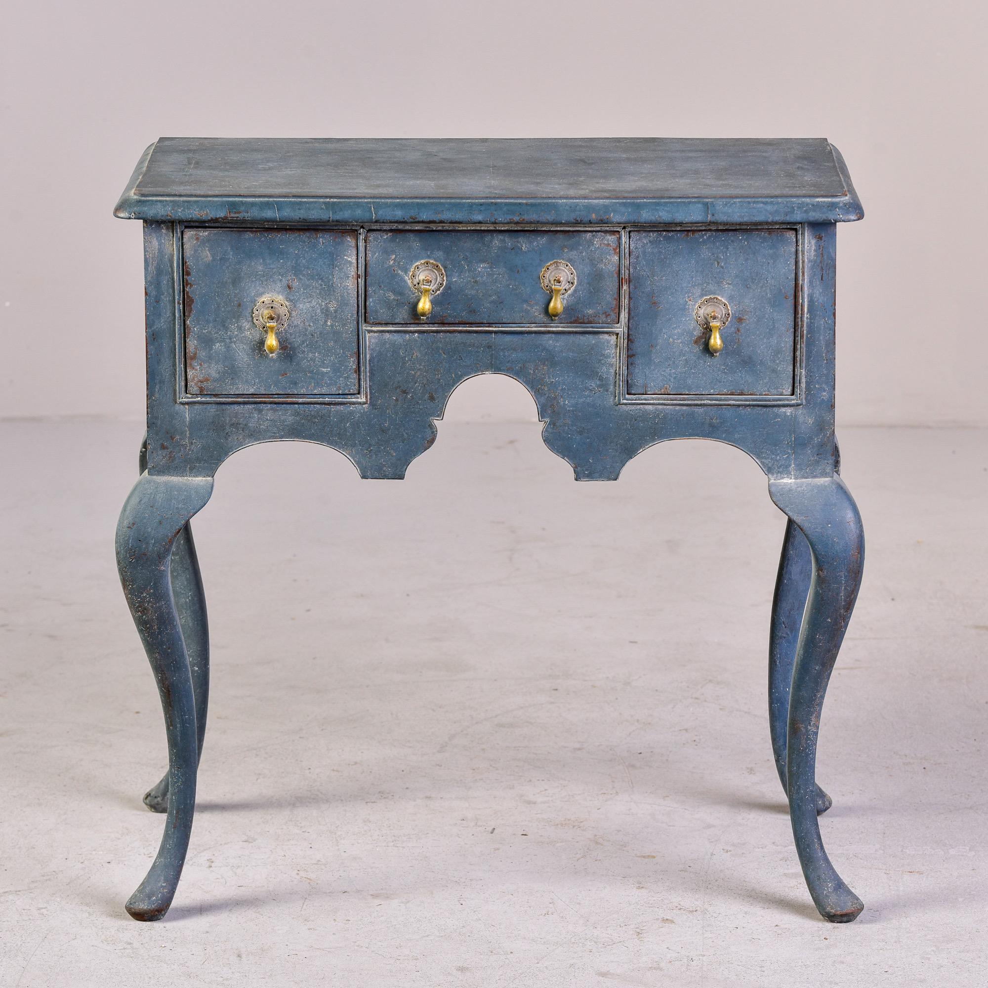 Circa 1760 English lamp table or lowboy features three functional drawers with brass hardware, a carved apron, curvy legs, and a blue painted finish. Unknown maker. Very good antique condition.