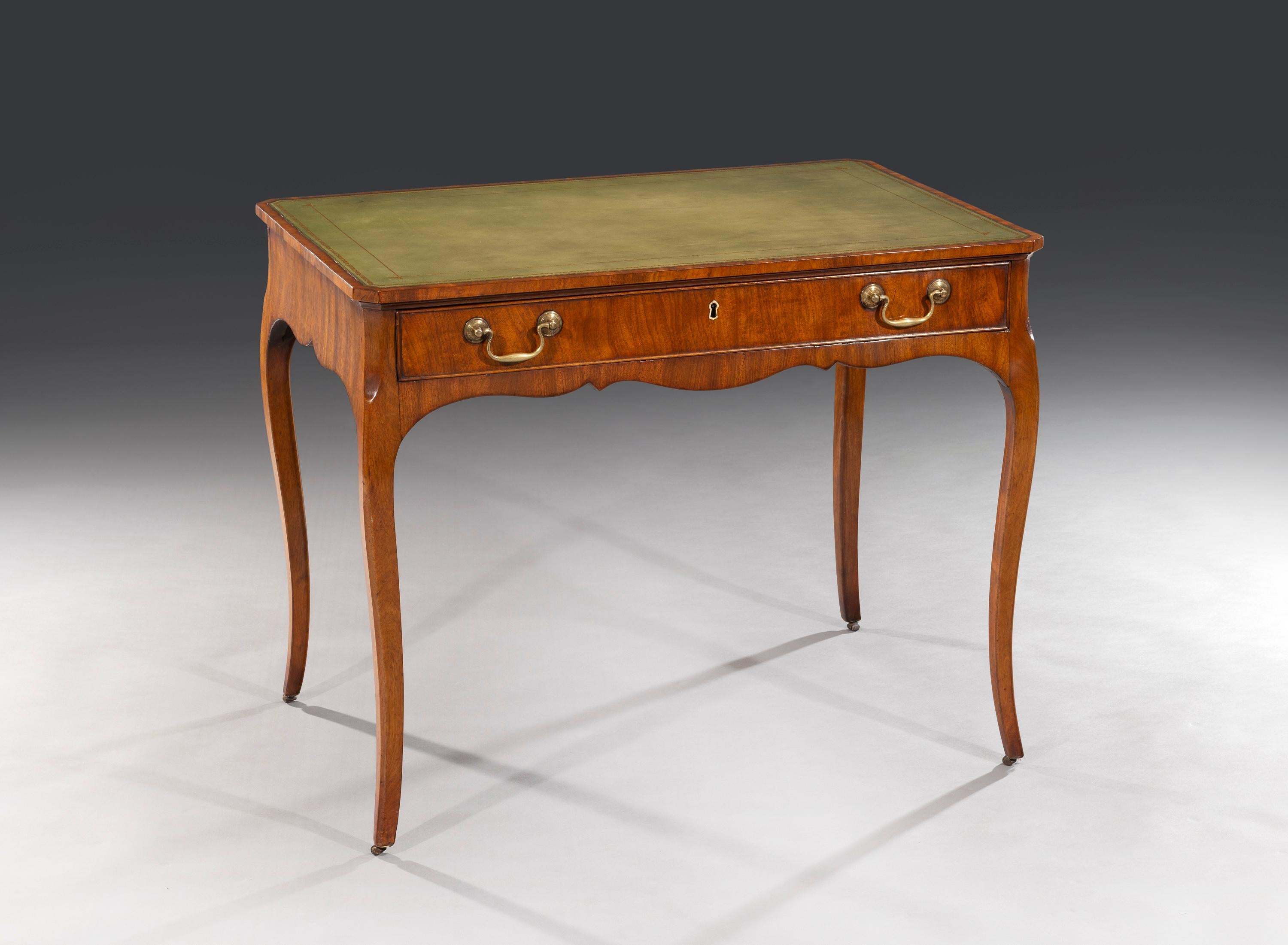 The mahogany writing table has recently been recovered with a light green leather top. The frieze is shaped and fitted with a single oak lined drawer which carries the original swan neck brass handles. The table stands on 'French Style' cabriole