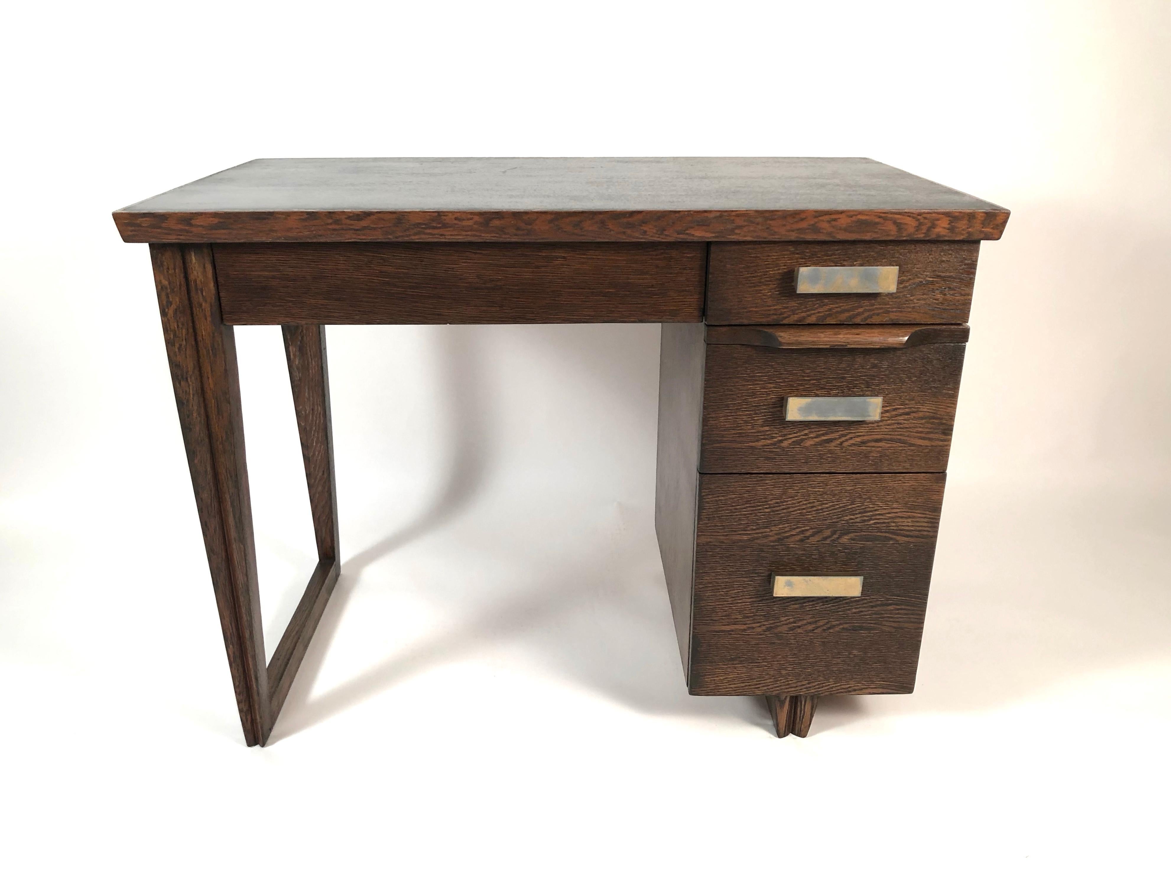 A stylish small and functional desk, American, circa 1940, in walnut stained oak with an ebonized top, with long drawer fitted with pen rest and other compartments, with three graduated drawers, the largest of which has dividers for files. Between