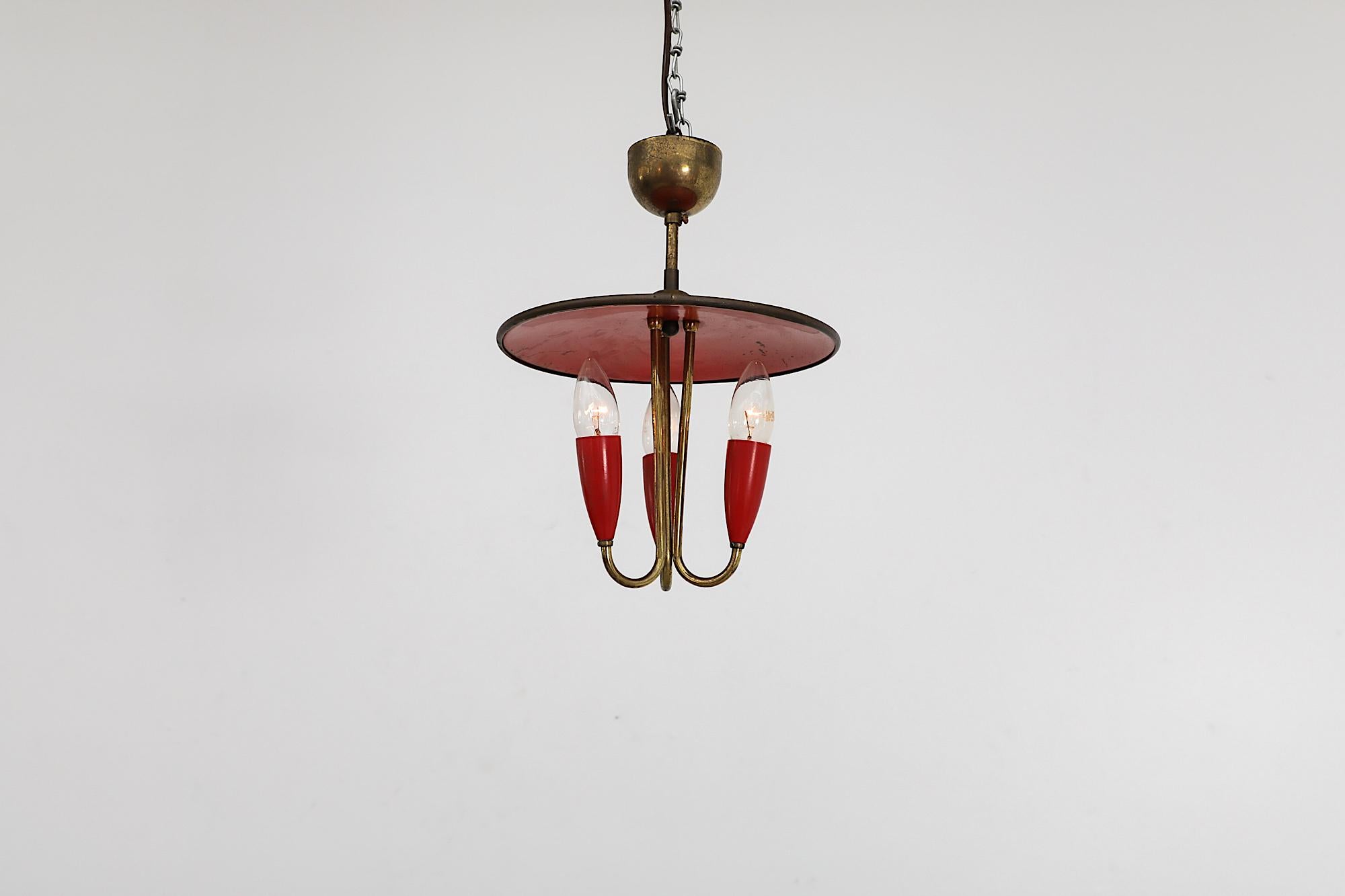 Beautiful brass Stilnovo Style three bulb chandelier with red enameled metal top shade and matching red socket holders. The lamp has EU candelabra sockets. In original condition with visible wear and patina, including tarnishing to the brass and