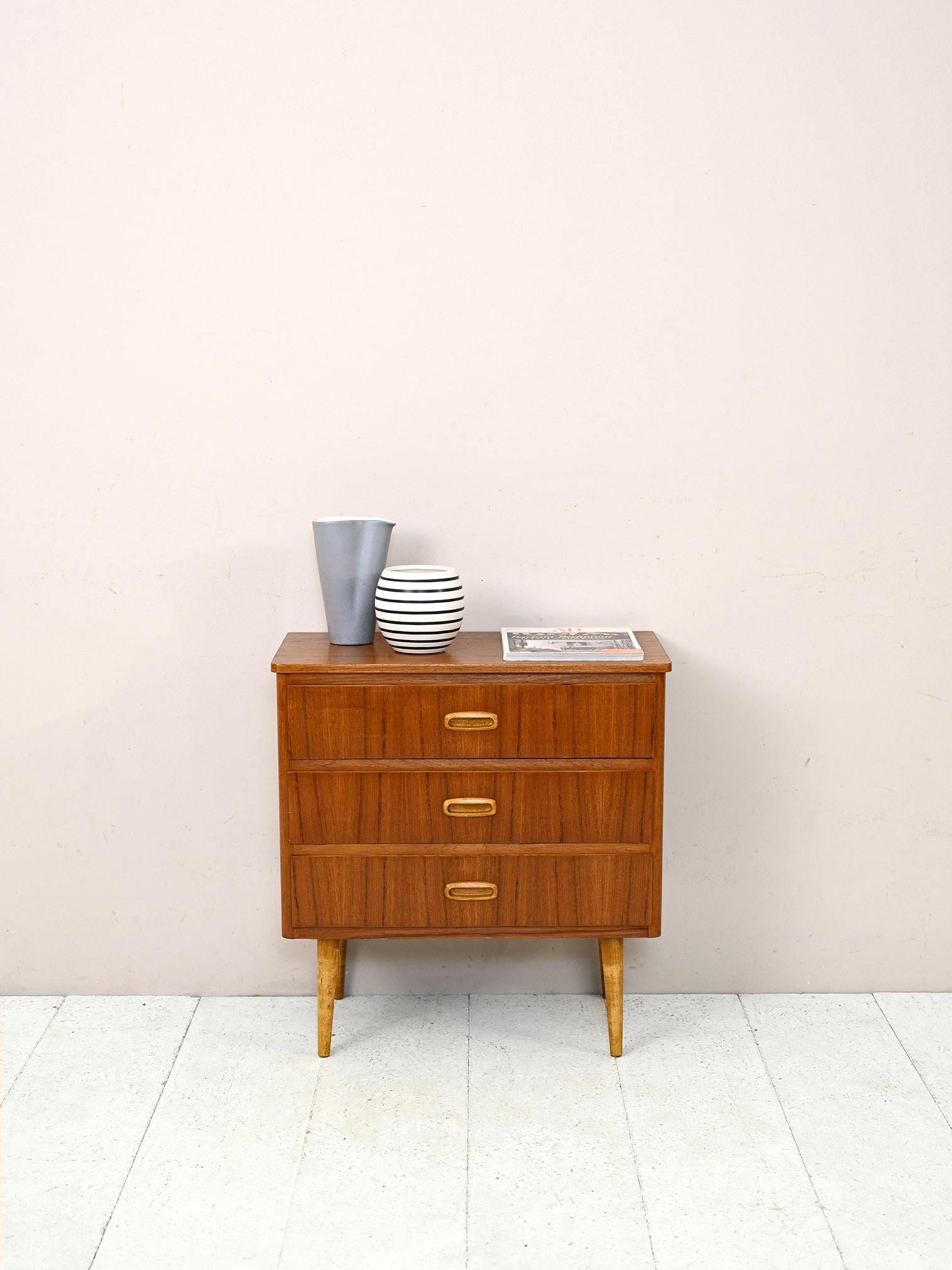 Swedish nightstand with three drawers.

A small chest of drawers, ideal for use as a nightstand or entryway cabinet.
The tapered legs and wood-carved drawer handles are distinctive features that harken back to mid-century Scandinavian
