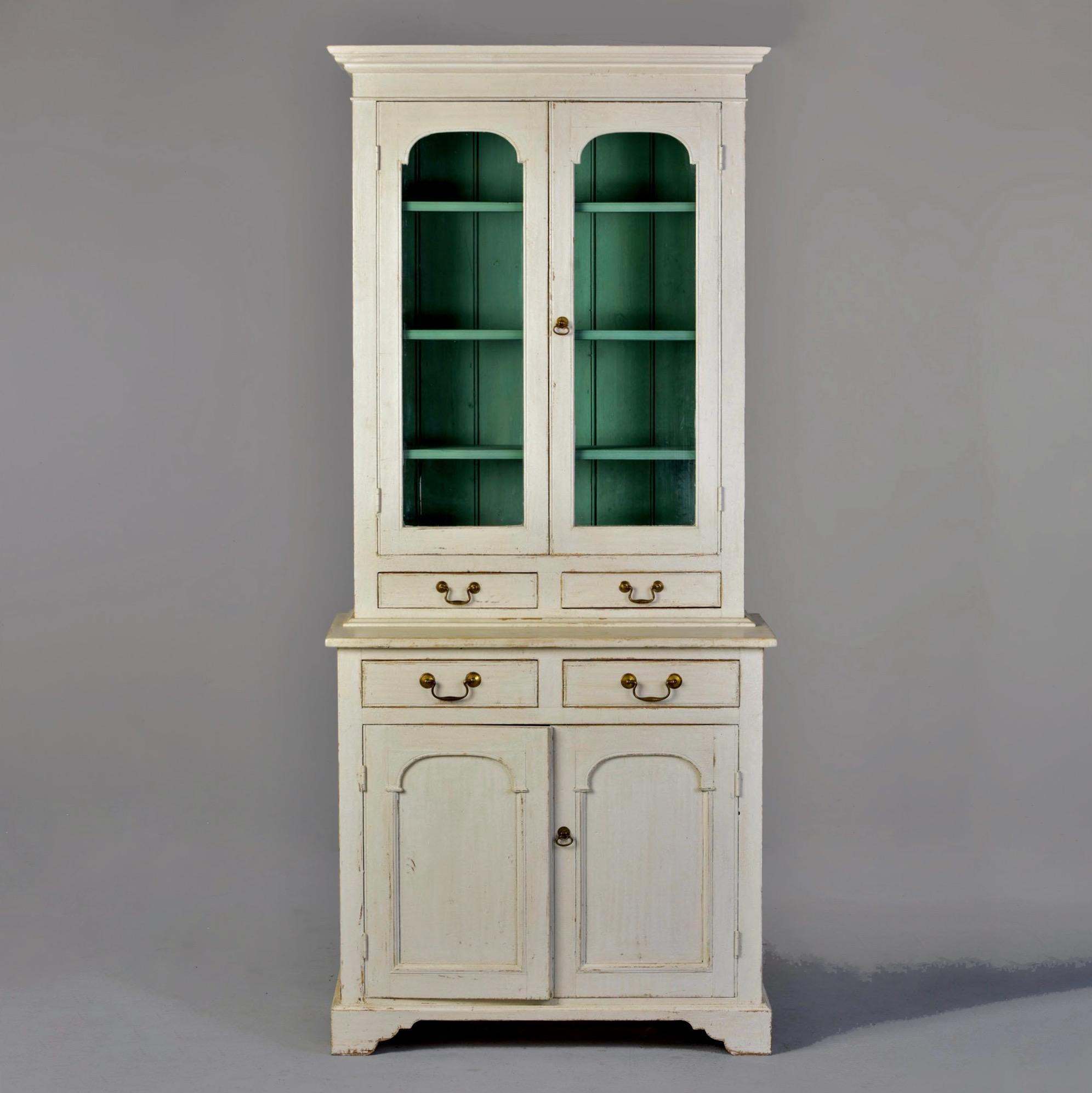 Circa 1880s two piece English bookcase with white painted finish. Top section is removable for shipping and features glazed doors with three internal shelves and two narrow drawers. Interior shelves and back painted contrasting blue/green. Footed