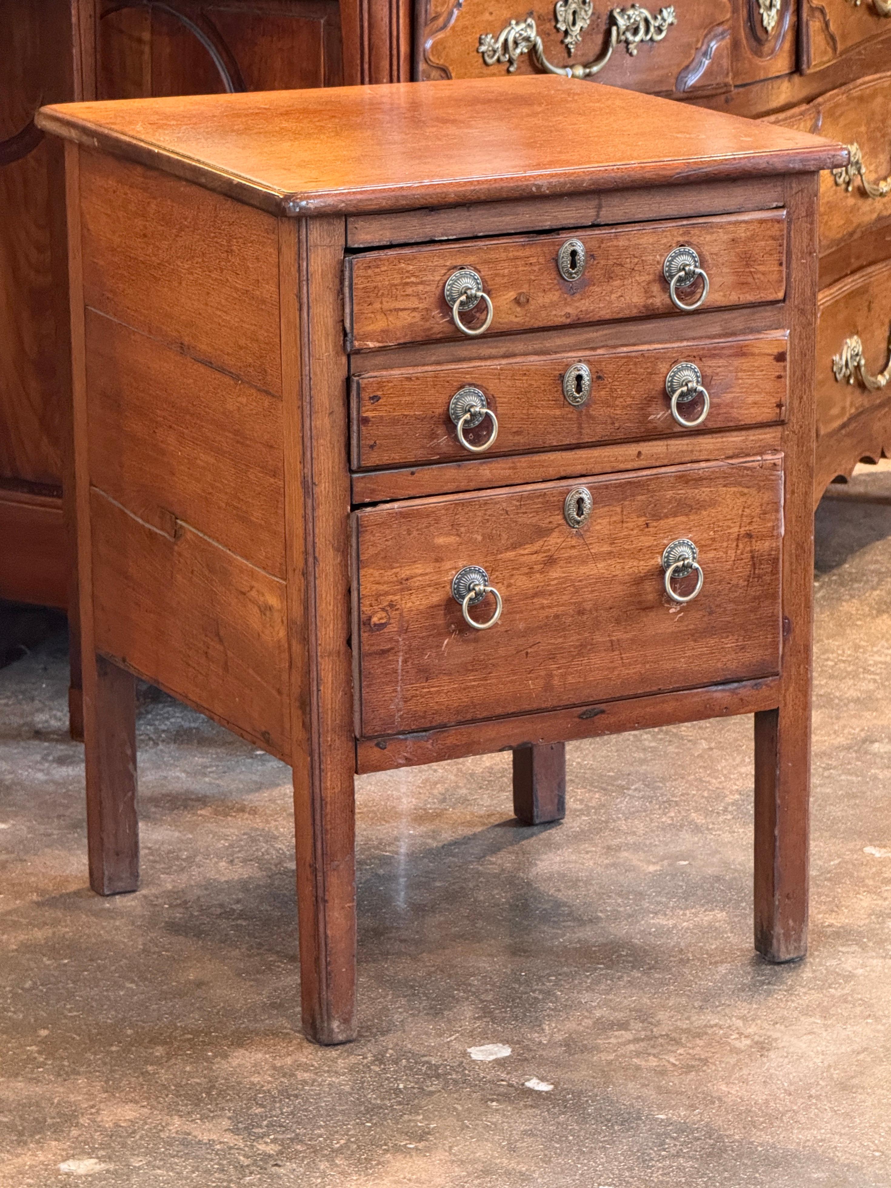 Late 19th century French walnut commode with three drawers and simple tapered legs. Retains its original ring pulls and brass escutcheons. Hand-cut dovetail joinery and warm patina throughout. Compact scale with clean lines and understated detailing.